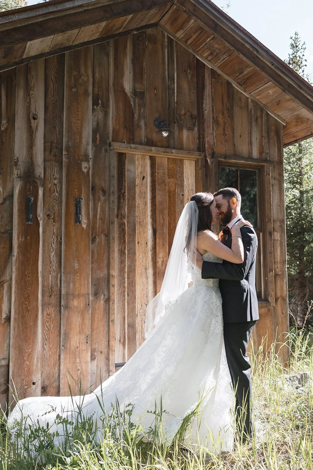 Bride and groom in wedding attire embracing after their first look with cabin behind