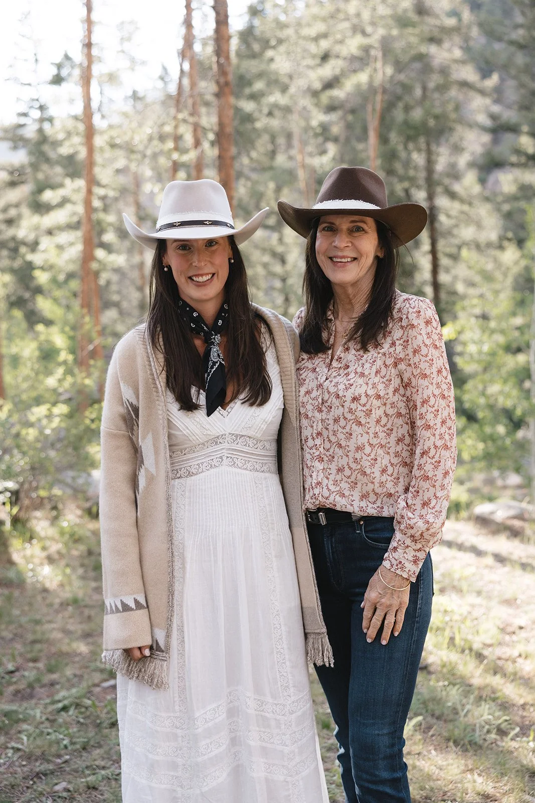 Bride in white western dress and cowgirl hat with her mother standing outside