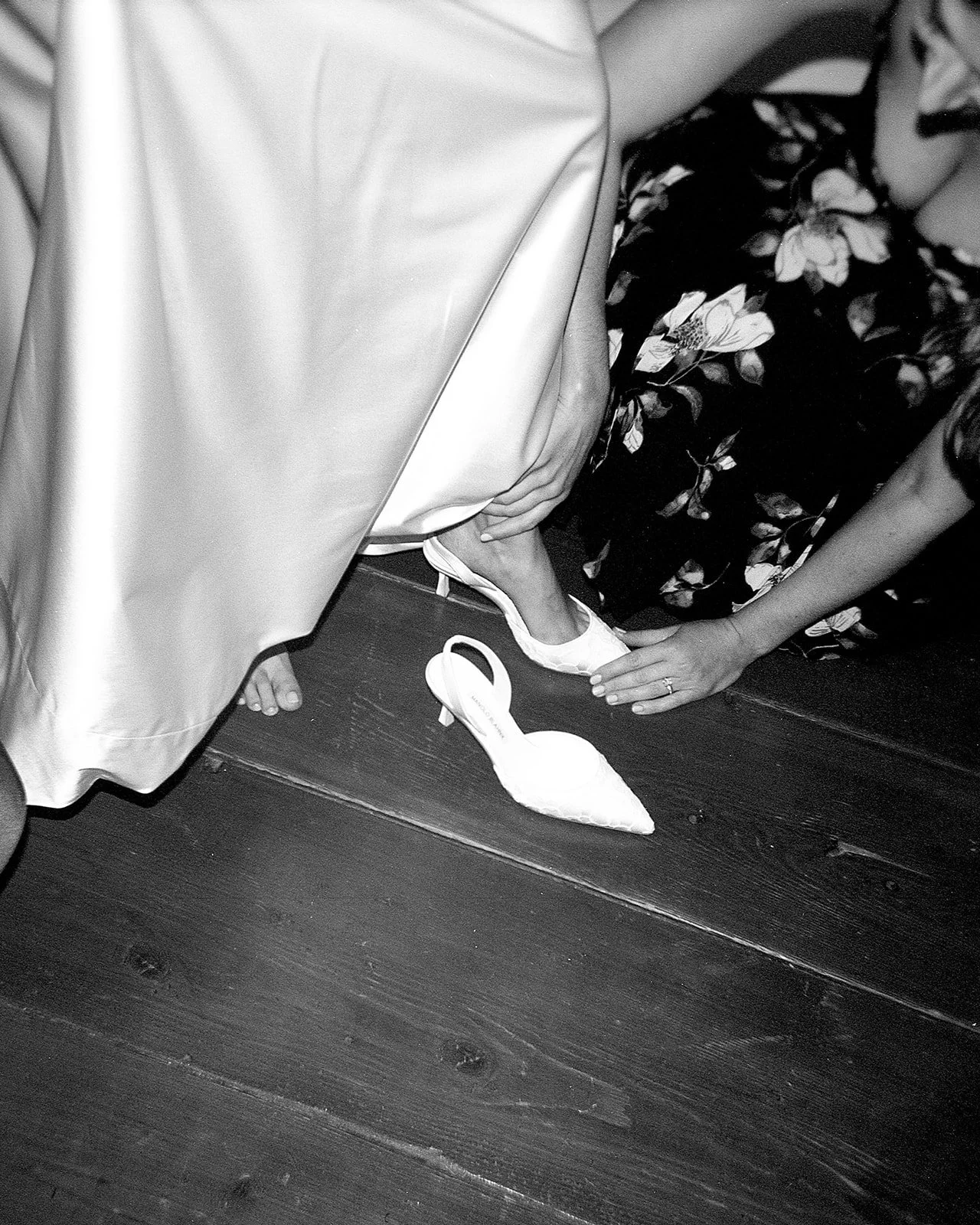 Bride putting on wedding shoes with help from friend