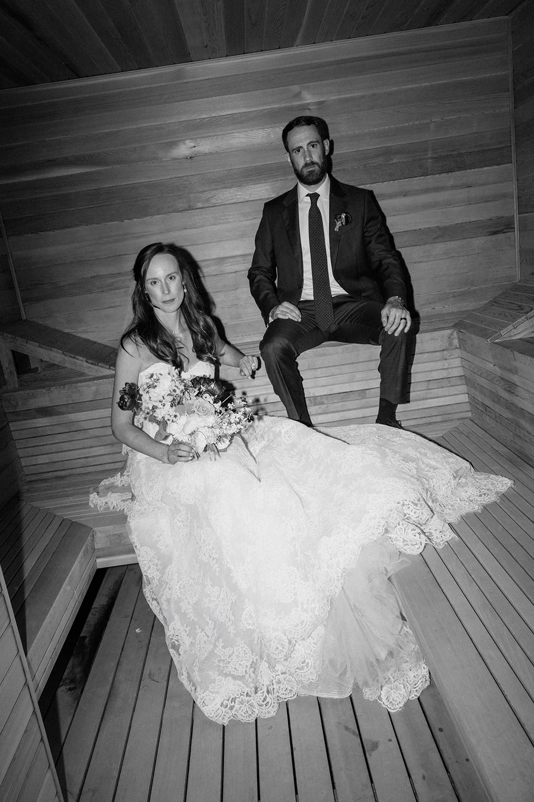 Bride and groom with serious faces looking at camera inside a wood sauna