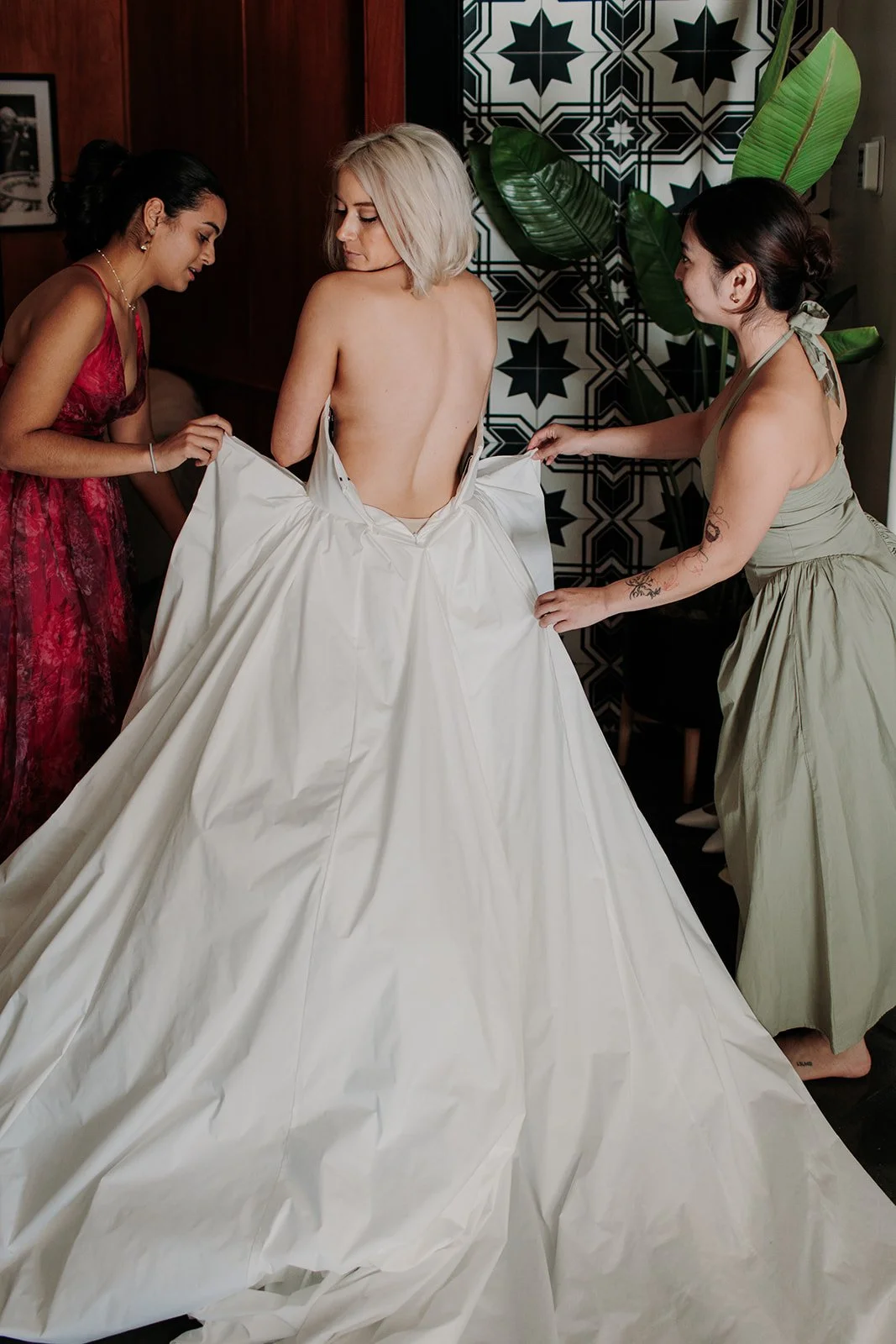 Bride wearing her dress with bridesmaids helping her