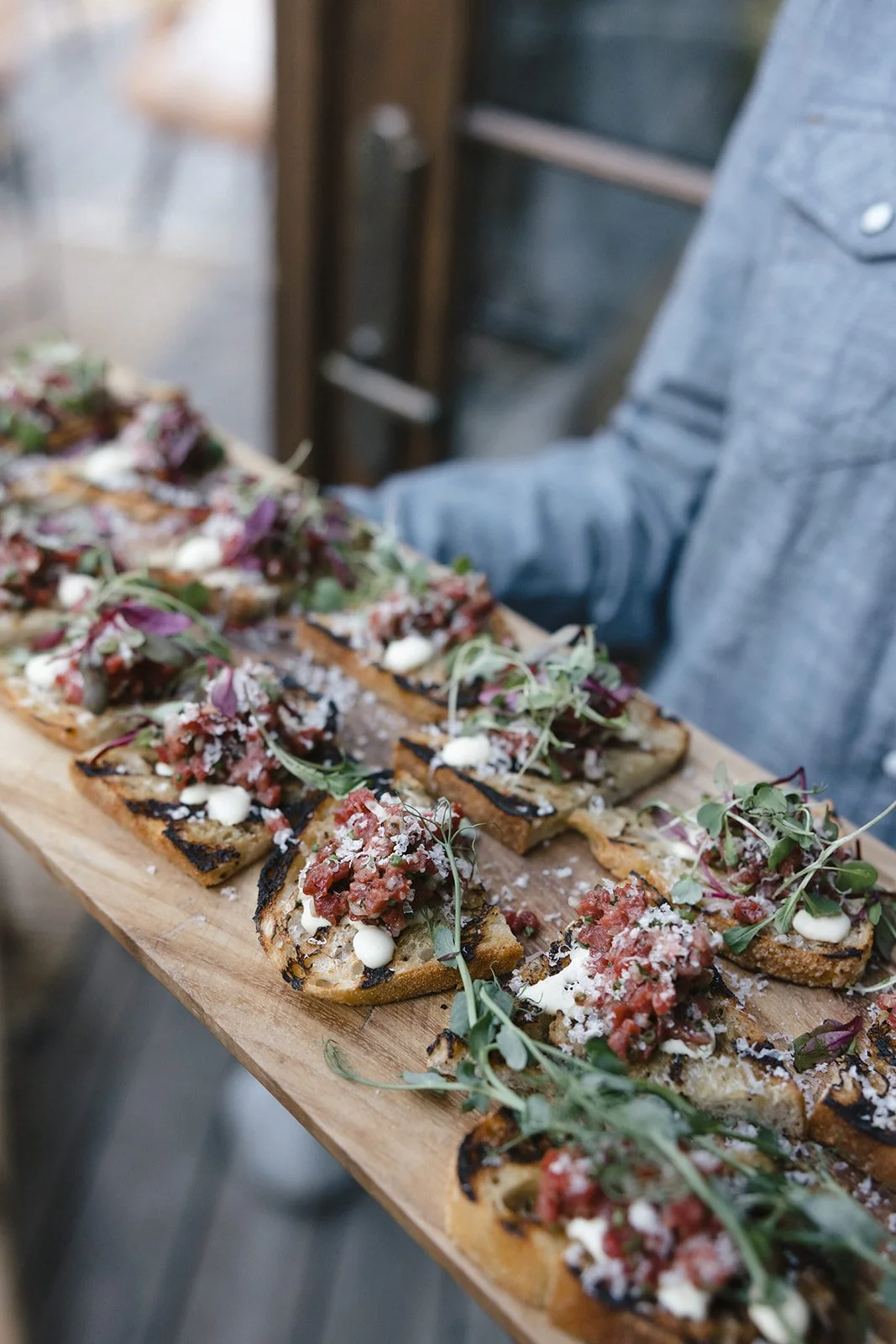 Appetizers of bread with toppings being passed on wood board