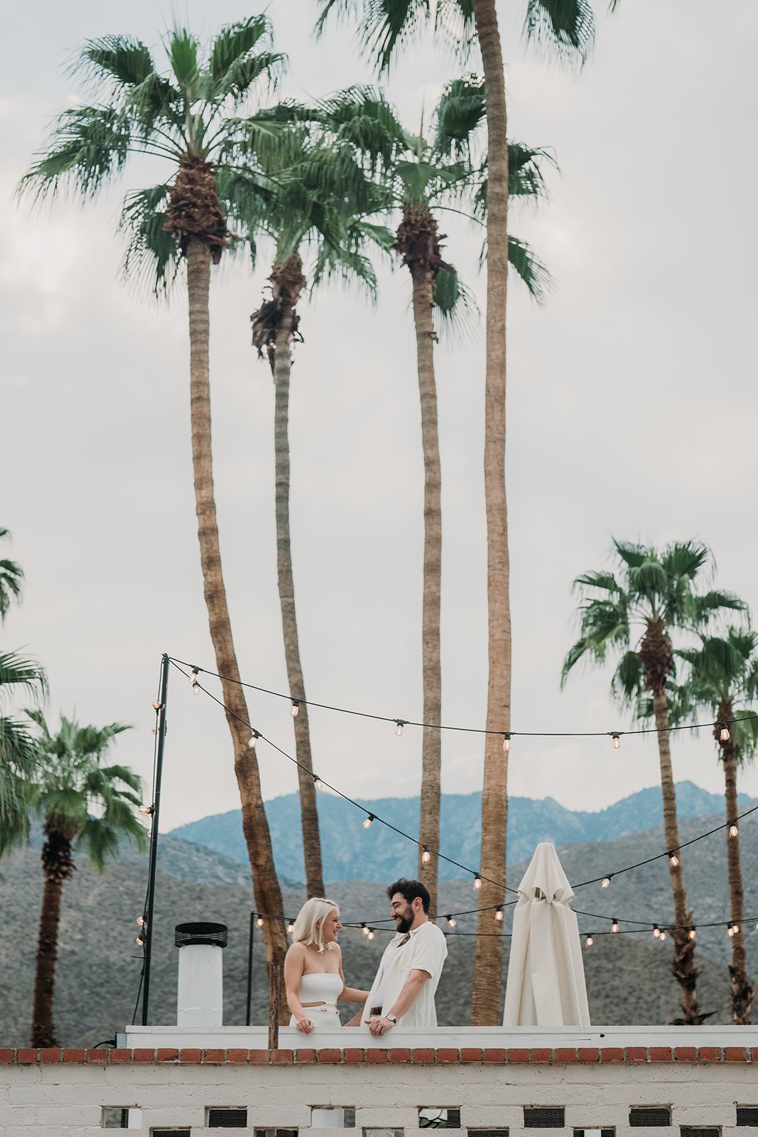 Bride and groom at welcome party on the roof with palms and mountains behind