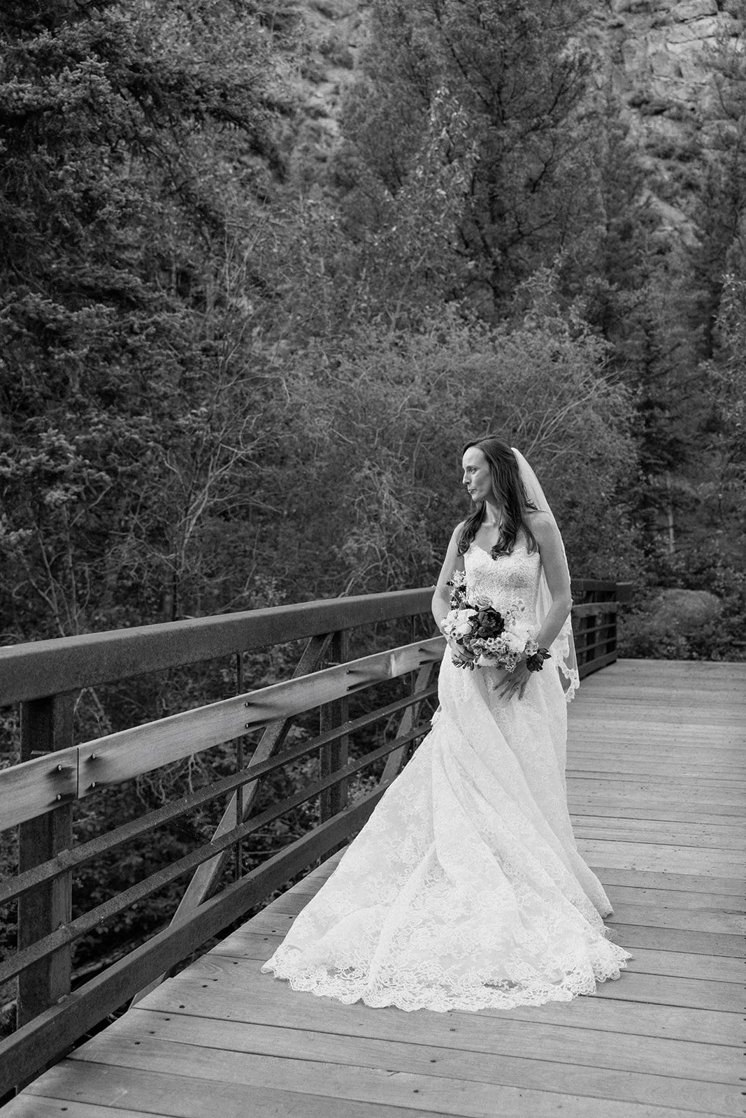 Bride standing on wooden bridge outside in wedding dress looking away from camera