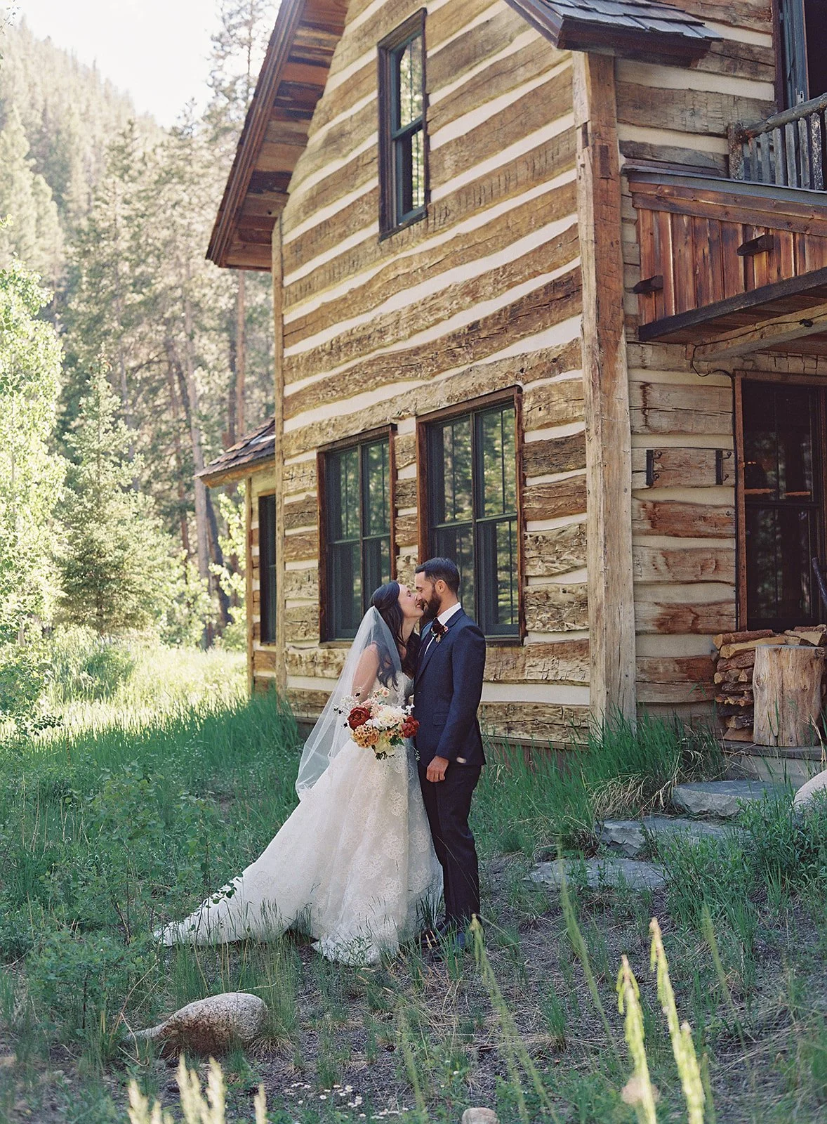 Bride and groom kissing with wedding attire on and outside of cabin
