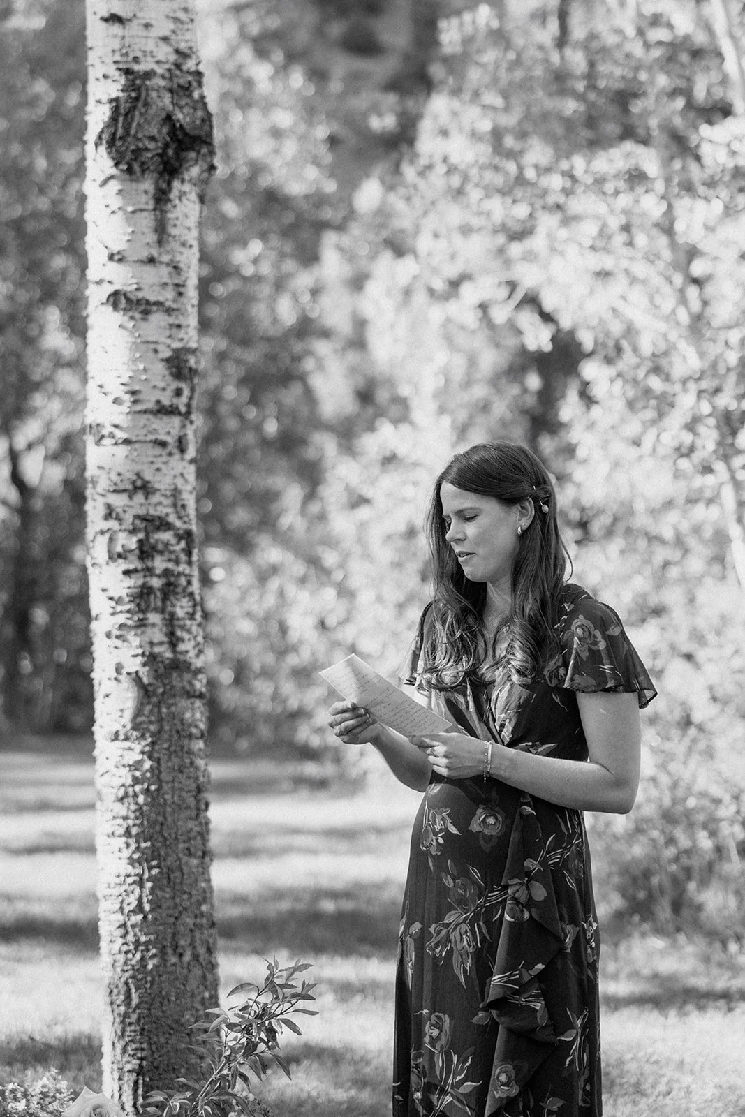 Wedding guest reading from paper at ceremony with trees behind her