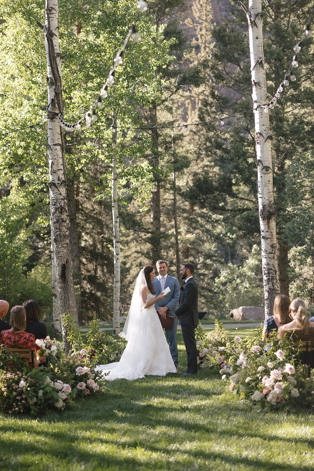 Bride and groom standing at altar in field with trees around them and officiant