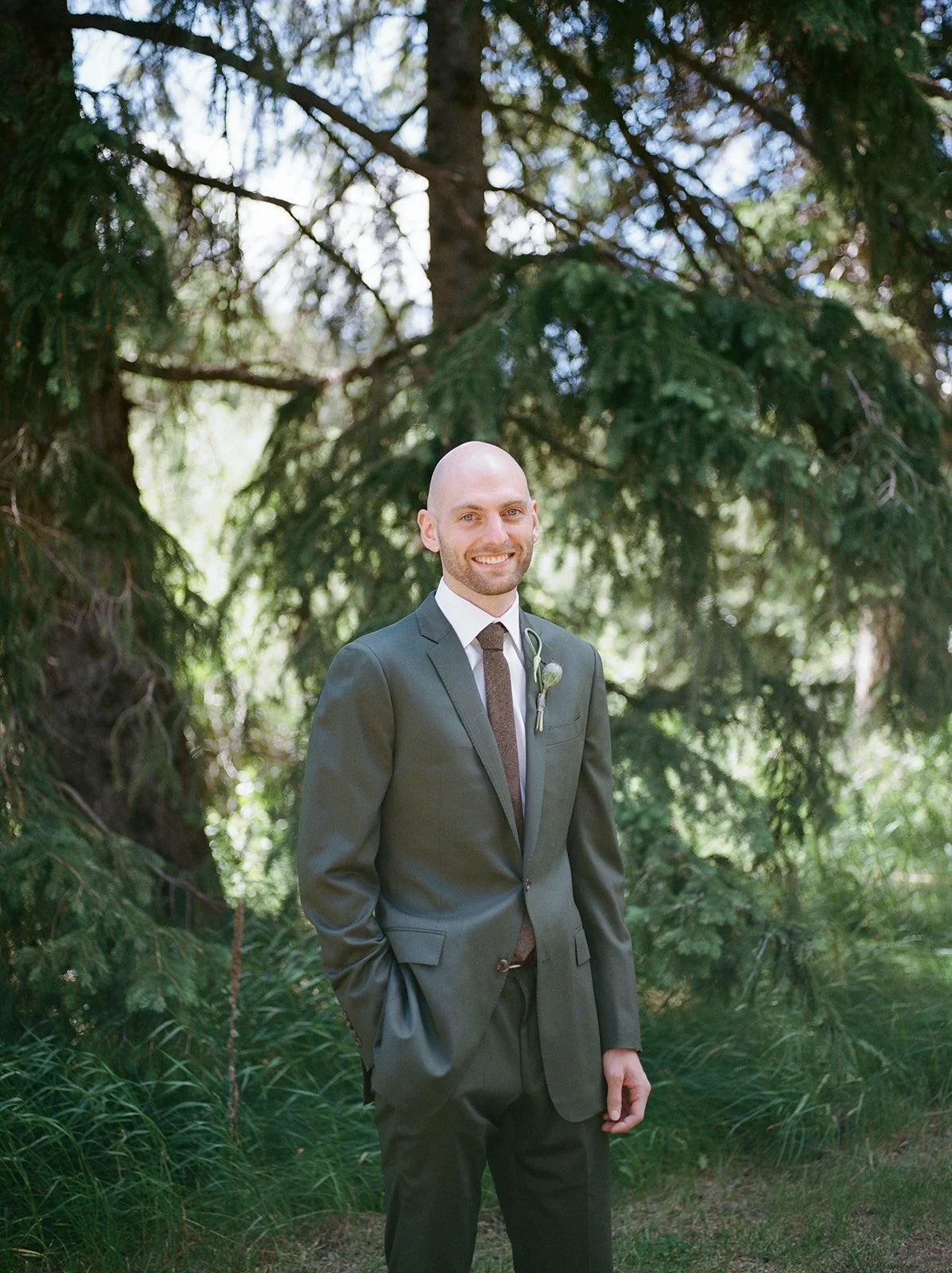 Groom with tux on in front of pine trees