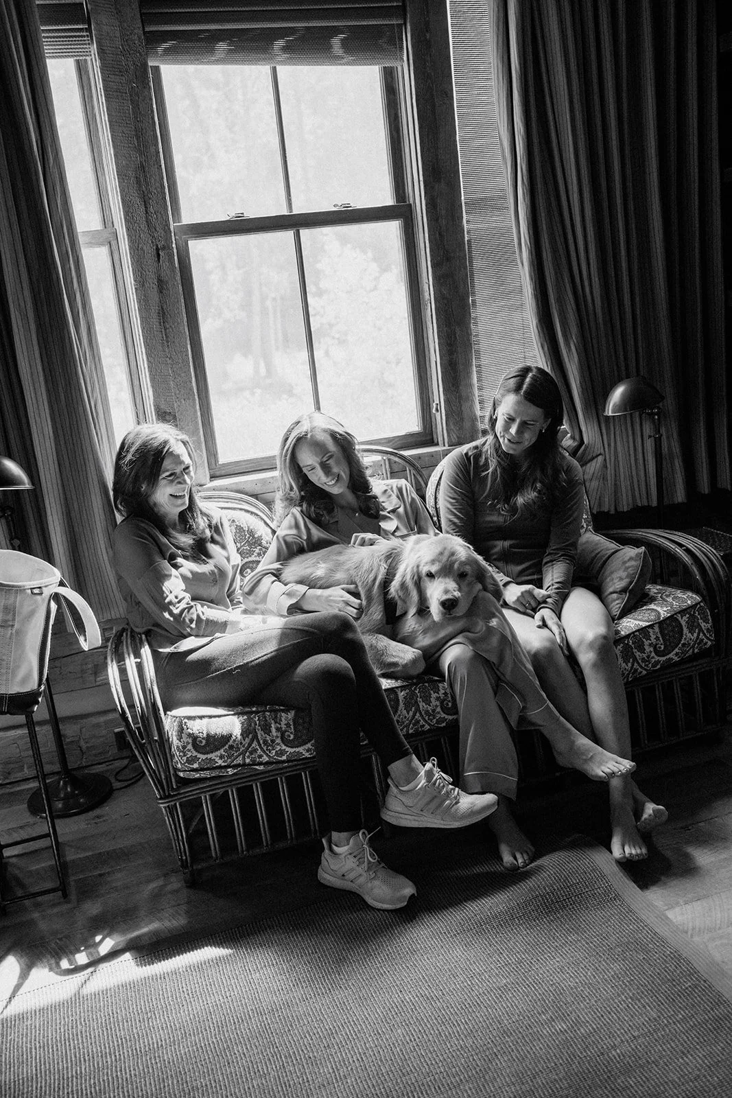 Bride, mom and sister sitting on a couch with dog on their laps smiling and laughing