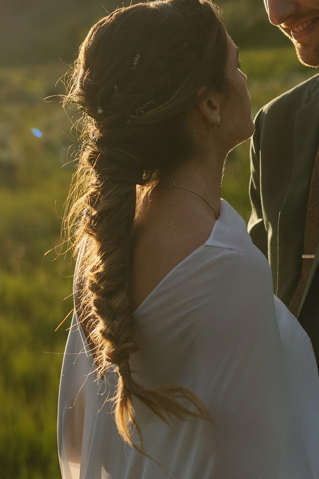 Brides long braid behind her back with groom leaning to kiss her