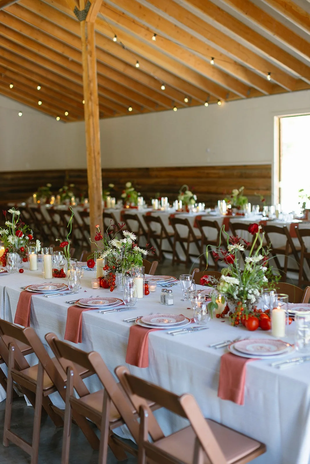 Reception table set for dinner inside barn with red florals