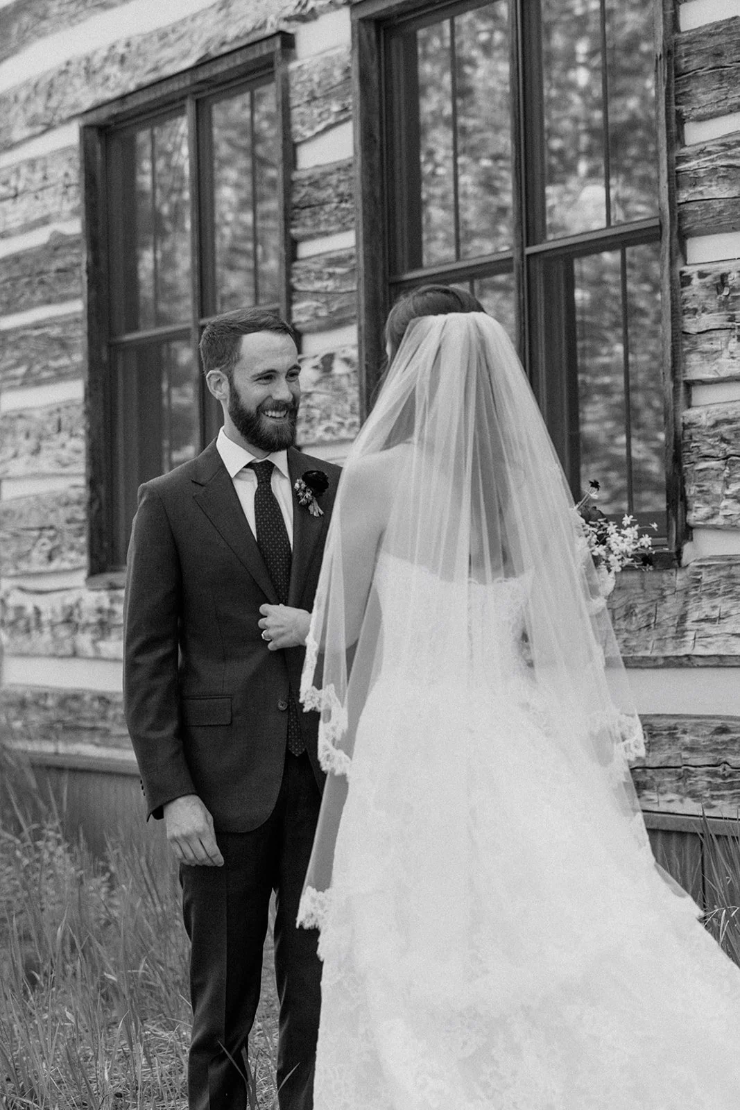 Groom smiling at the bride with her back to camera and veil and dress