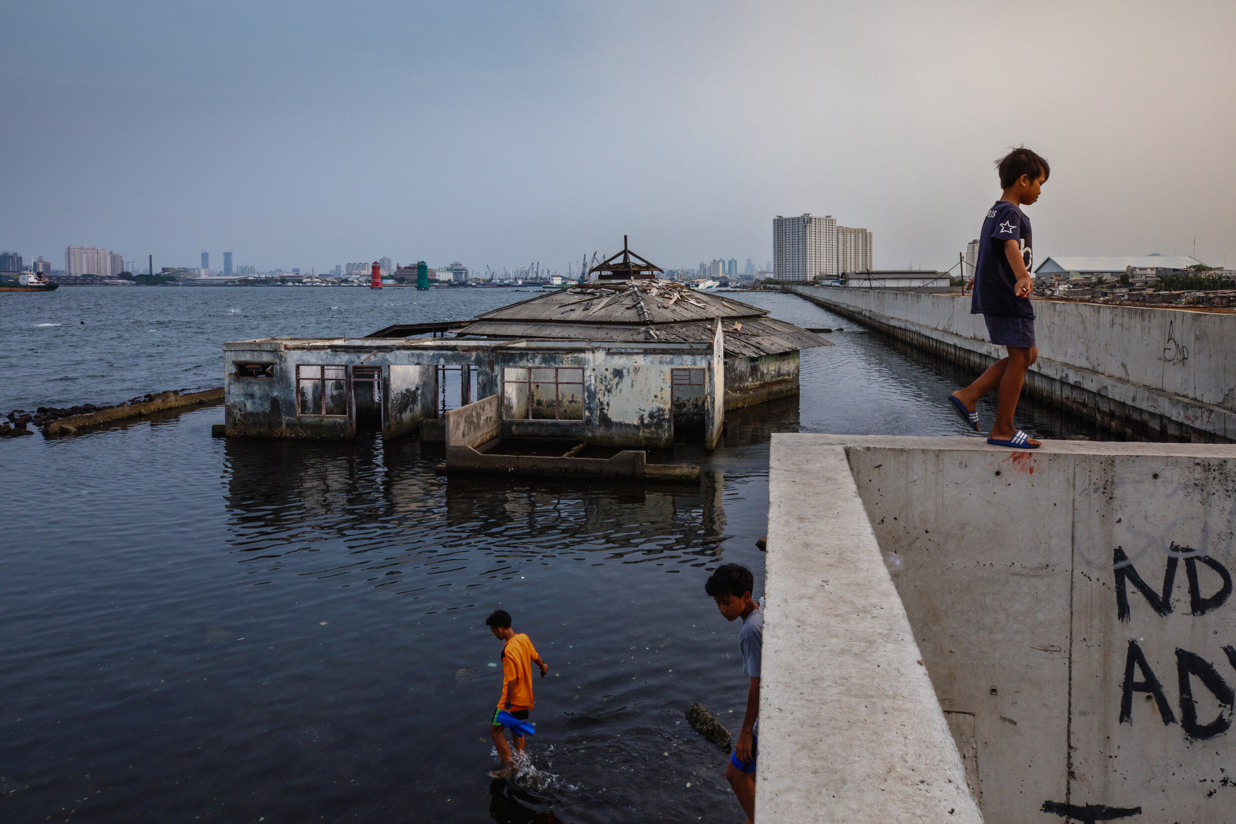  A boy walks on the newly built sea wall that is next to the  Waladuna Mosque, now partially submerged in seawater, and has become a symbol of the sinking city of Jakarta/ Indonesia - 2019 