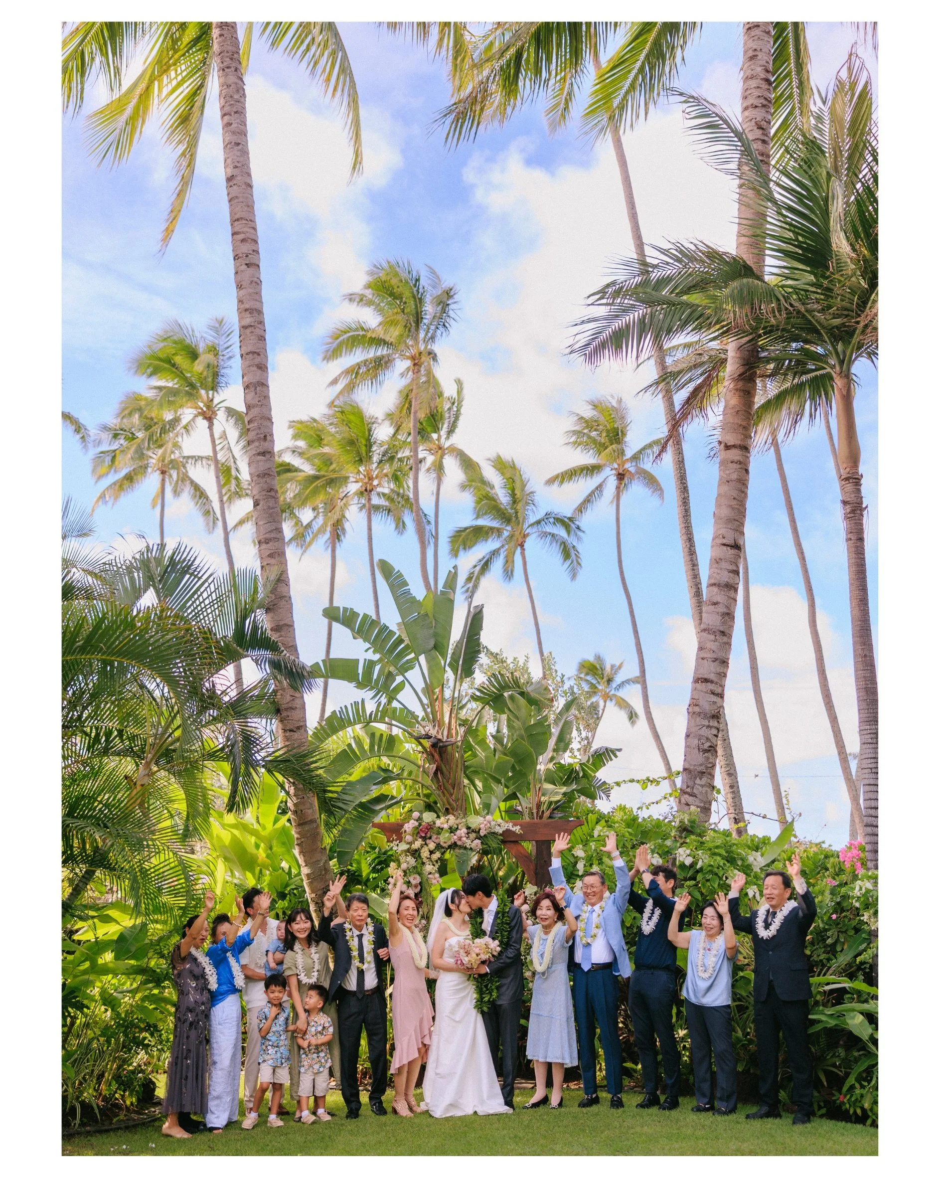 Tiffany and Sungho kissing during a family portrait as their loved ones cheer at Male'ana Gardens in Kailua, Oahu