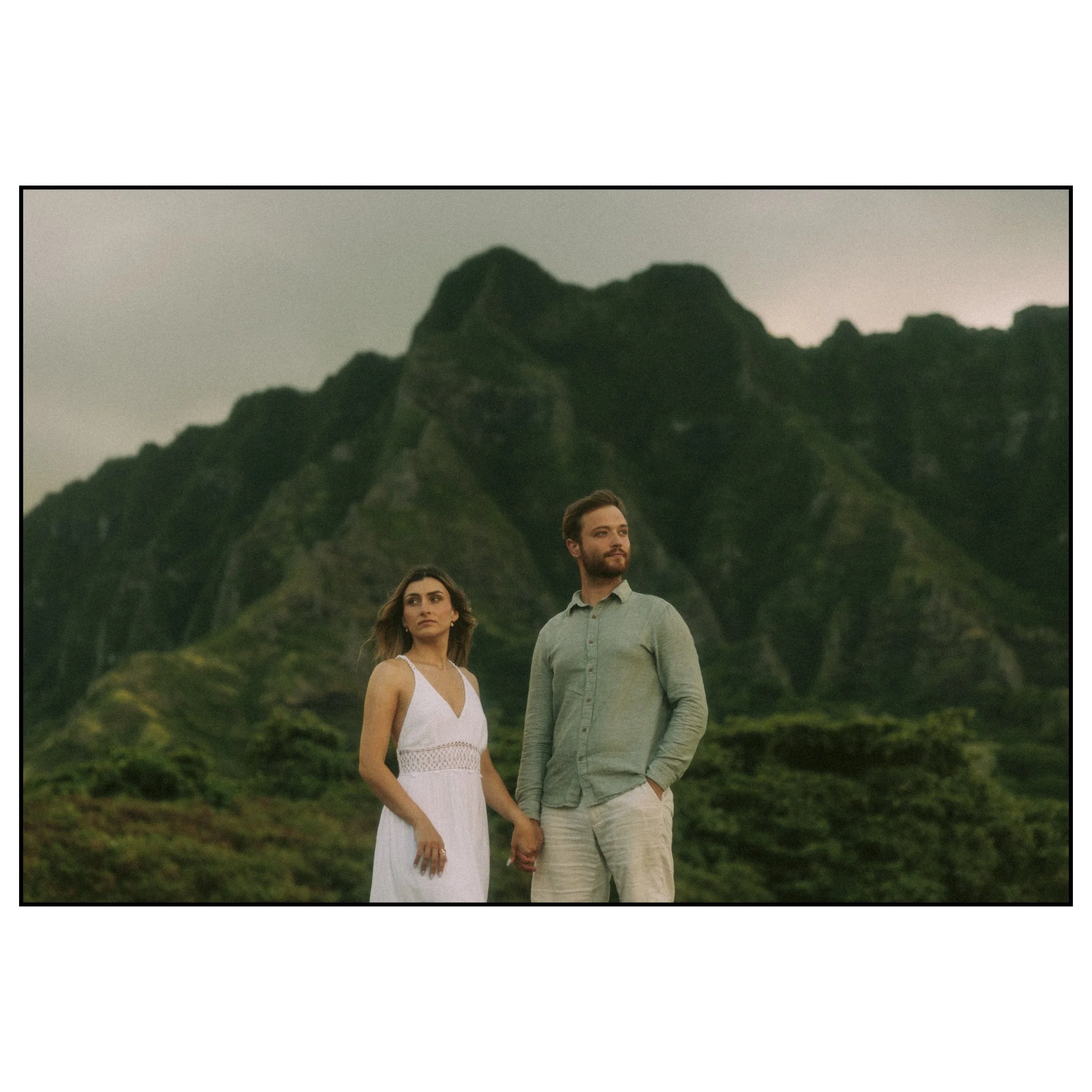 Couple standing beneath the dramatic Koʻolau mountains during a cinematic couples session at Kualoa Regional Park on Oahu.