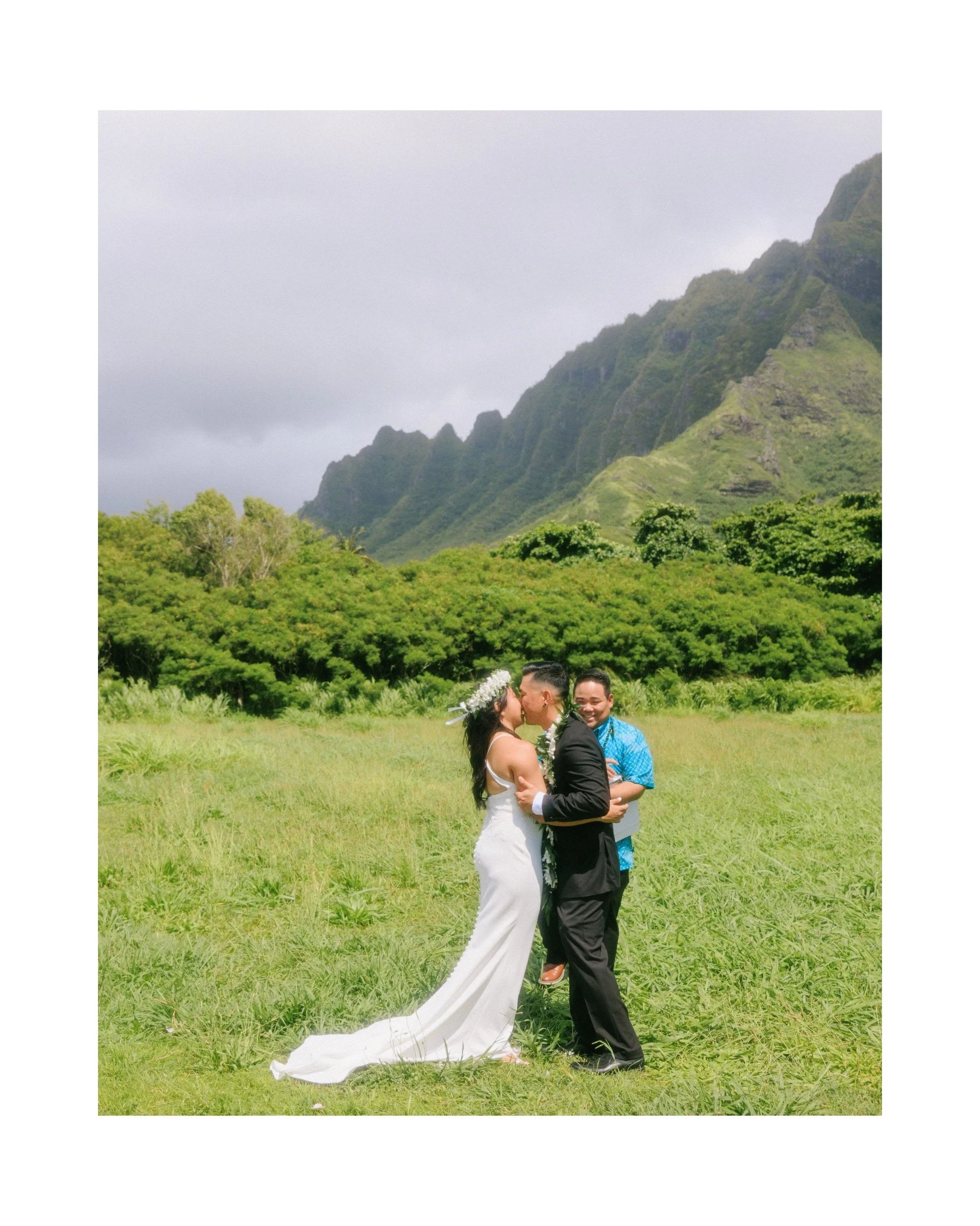 Alexis and Brede sharing their first kiss during their outdoor Hawaii elopement ceremony at Kualoa Regional Park with dramatic Koʻolau mountain views behind them.