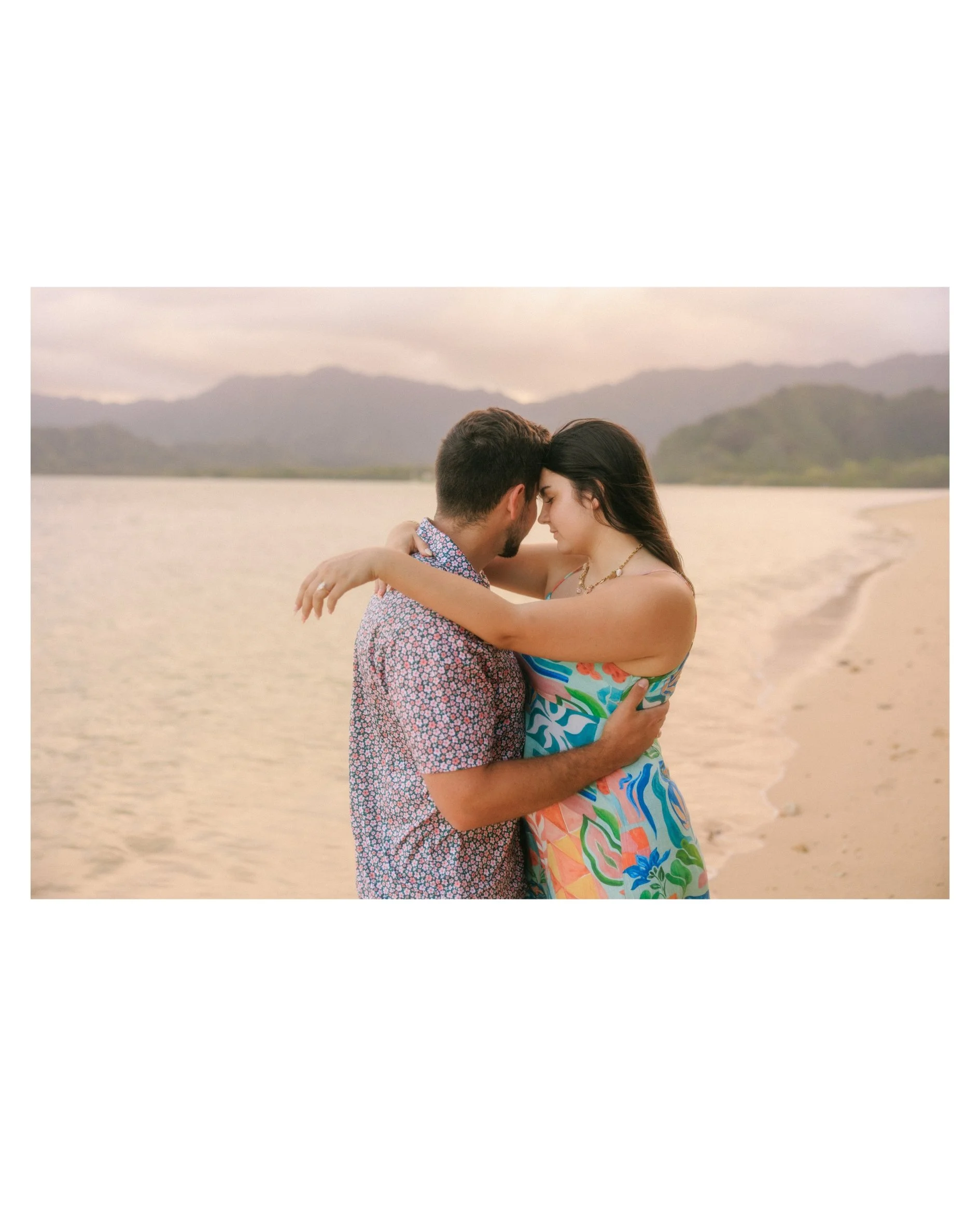 Intimate sunset engagement session at Kualoa Regional Park with Jake and Sloane embracing on the beach after their surprise proposal on Oahu, Hawaii with soft golden light and mountain views.