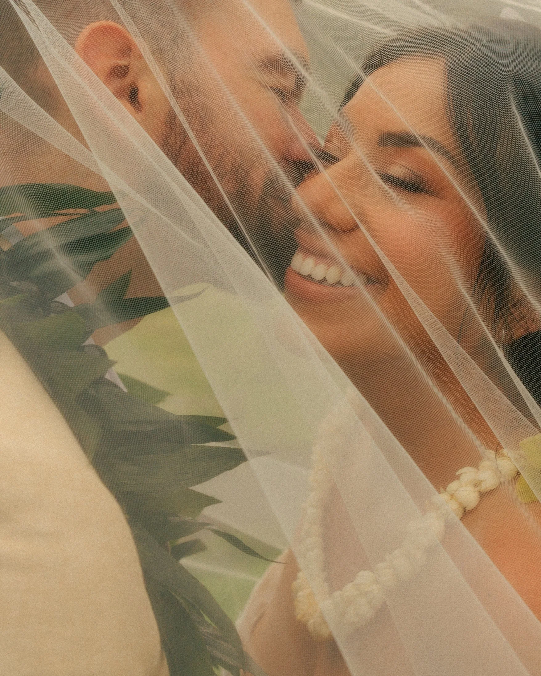 A close-up of Nicole smiling under her sheer veil beside Ethan, both wearing lei, in an intimate cinematic portrait from their elopement at Paliku Gardens, Kualoa Ranch, on Oahu, Hawaii.