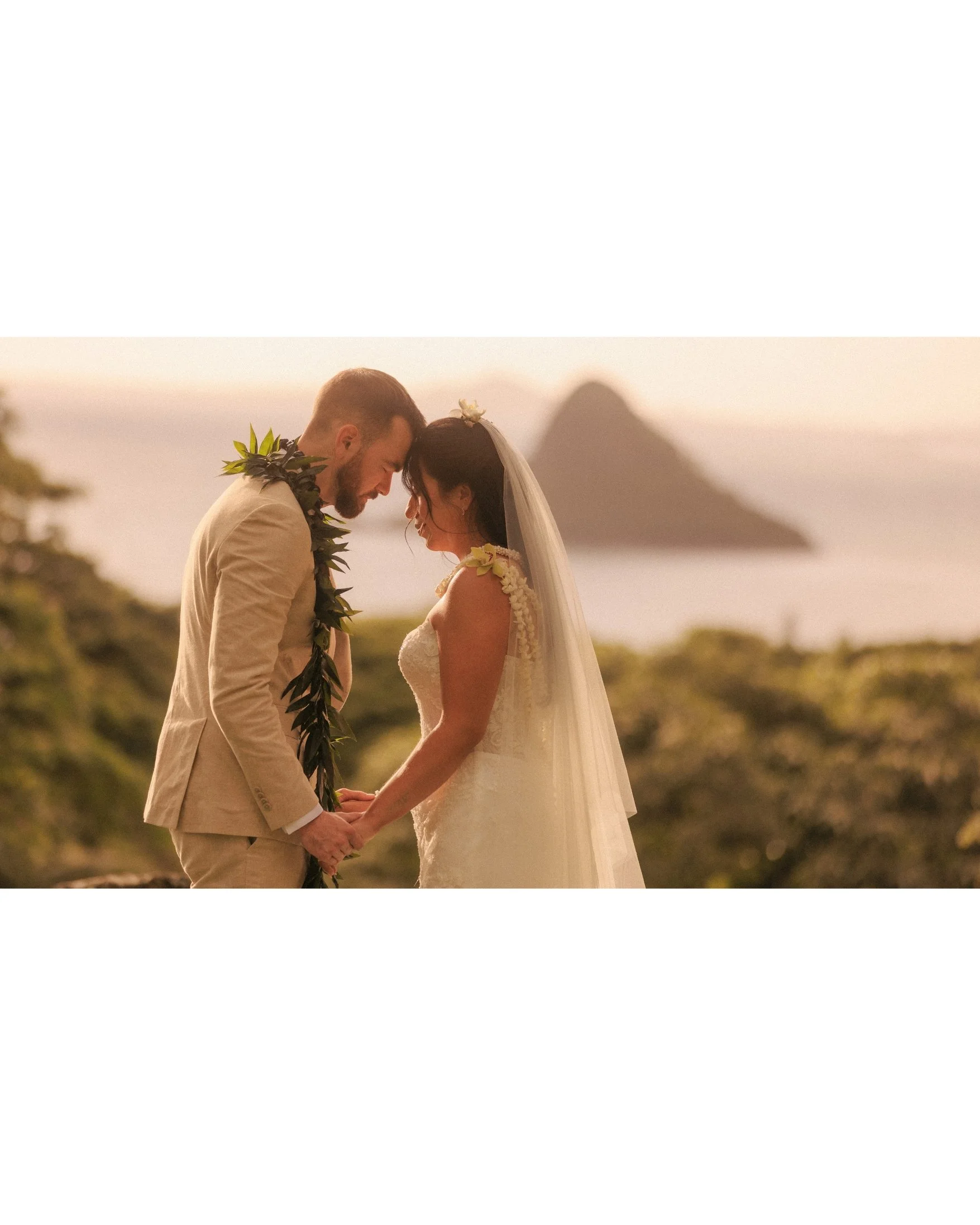 Nicole and Ethan hold hands with their foreheads touching in soft sunrise light at Paliku Gardens, Kualoa Ranch, with Mokoli'i island rising from the ocean behind them on Oahu, Hawaii.