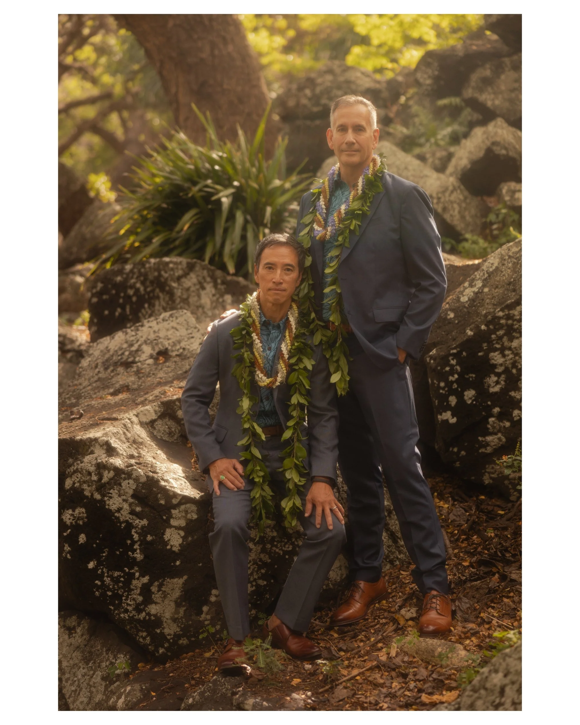 Portrait of a married couple wearing Hawaiian leis among moss covered boulders during a portrait session at Liliʻuokalani Botanical Garden in Honolulu, Hawaii. Romantic wedding portrait photographed by an Oahu wedding photographer.