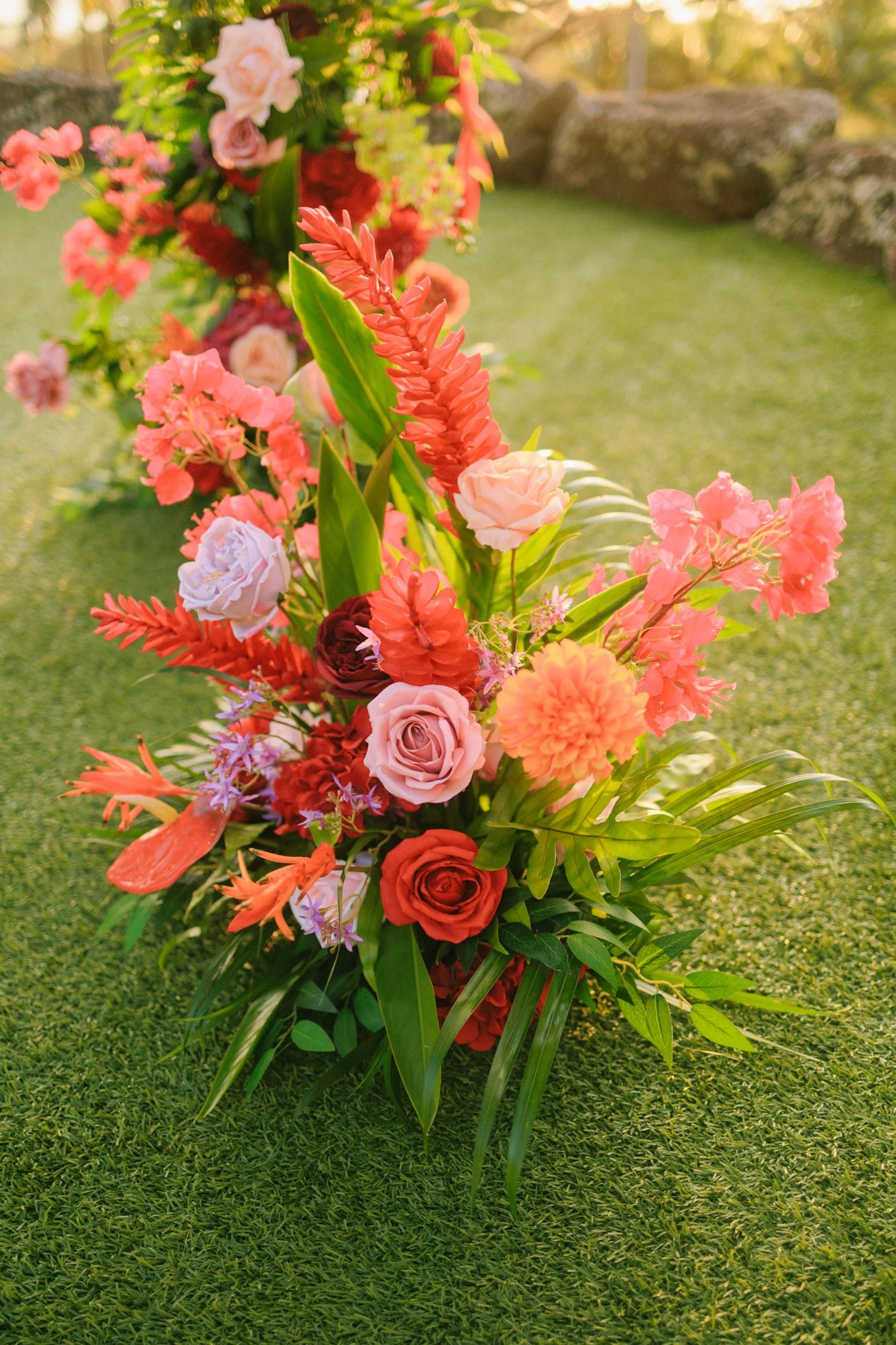 Colorful floral arrangement with roses, dahlias, and greenery on a green surface outdoors.