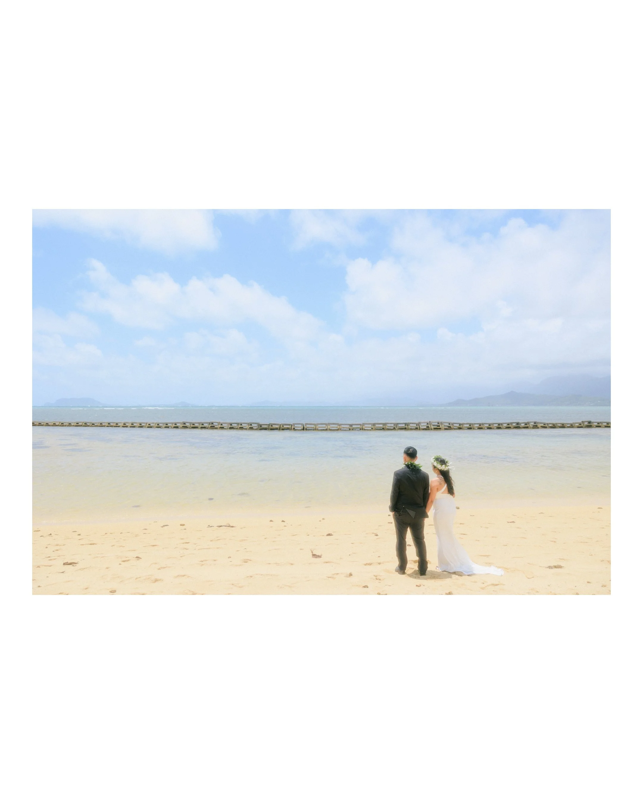 Newly married couple standing together on the beach at Kualoa Regional Park overlooking the ocean during their relaxed Hawaii elopement on Oahu.