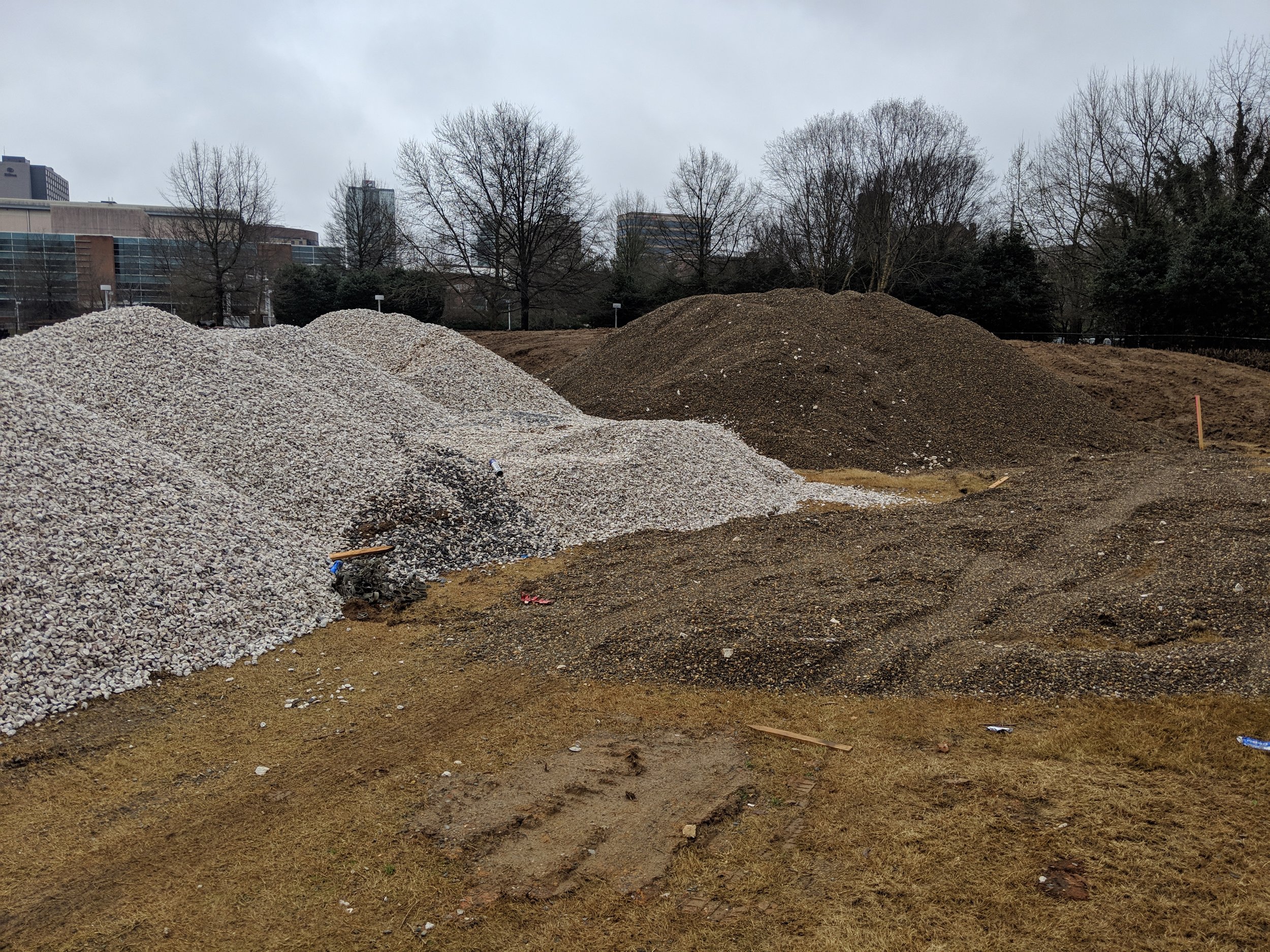 New gravel is stockpiled adjacent to gravel salvaged from the site during demolition. These stockpiles will be used around the lawn's under-drain system.