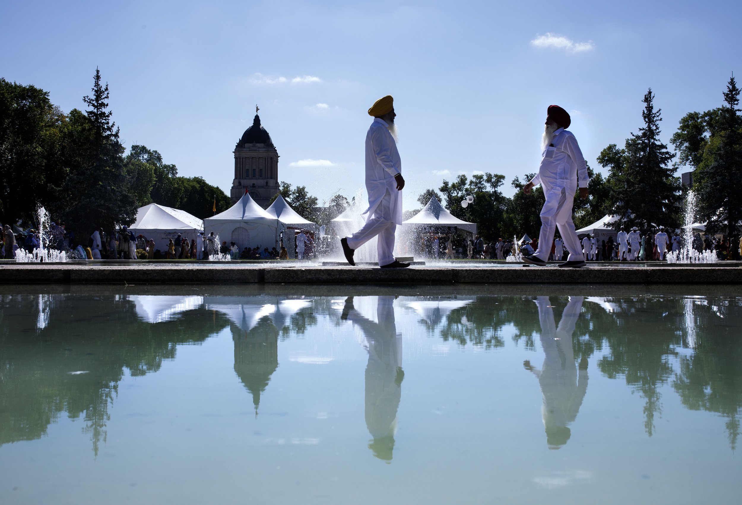 Sikh men in silhouette walk past water and tents on a bright summer blue sky