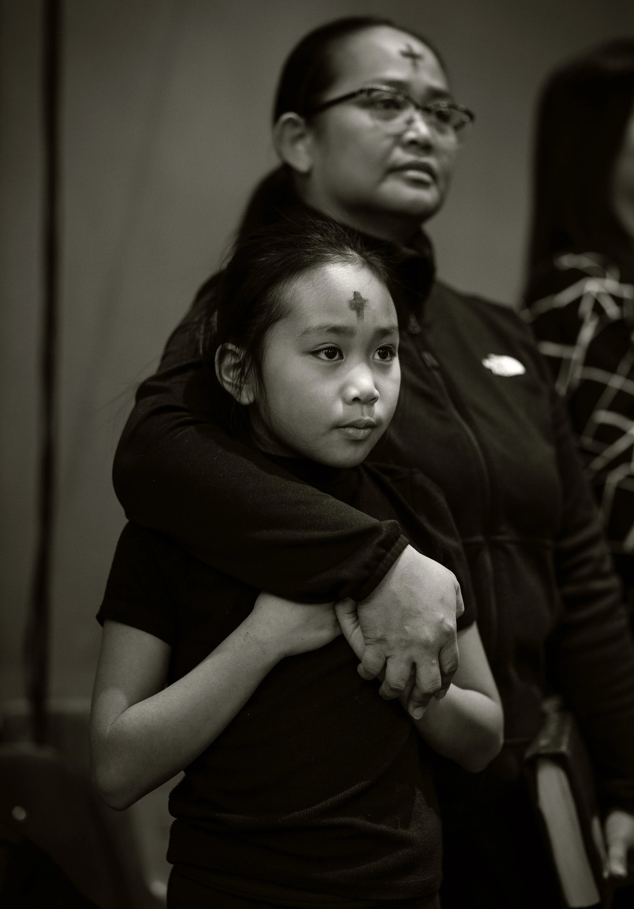 Filipino girl is embraced by mother both with ash cross marked on their foreheads during Ash Wednesday church service in Winnipeg