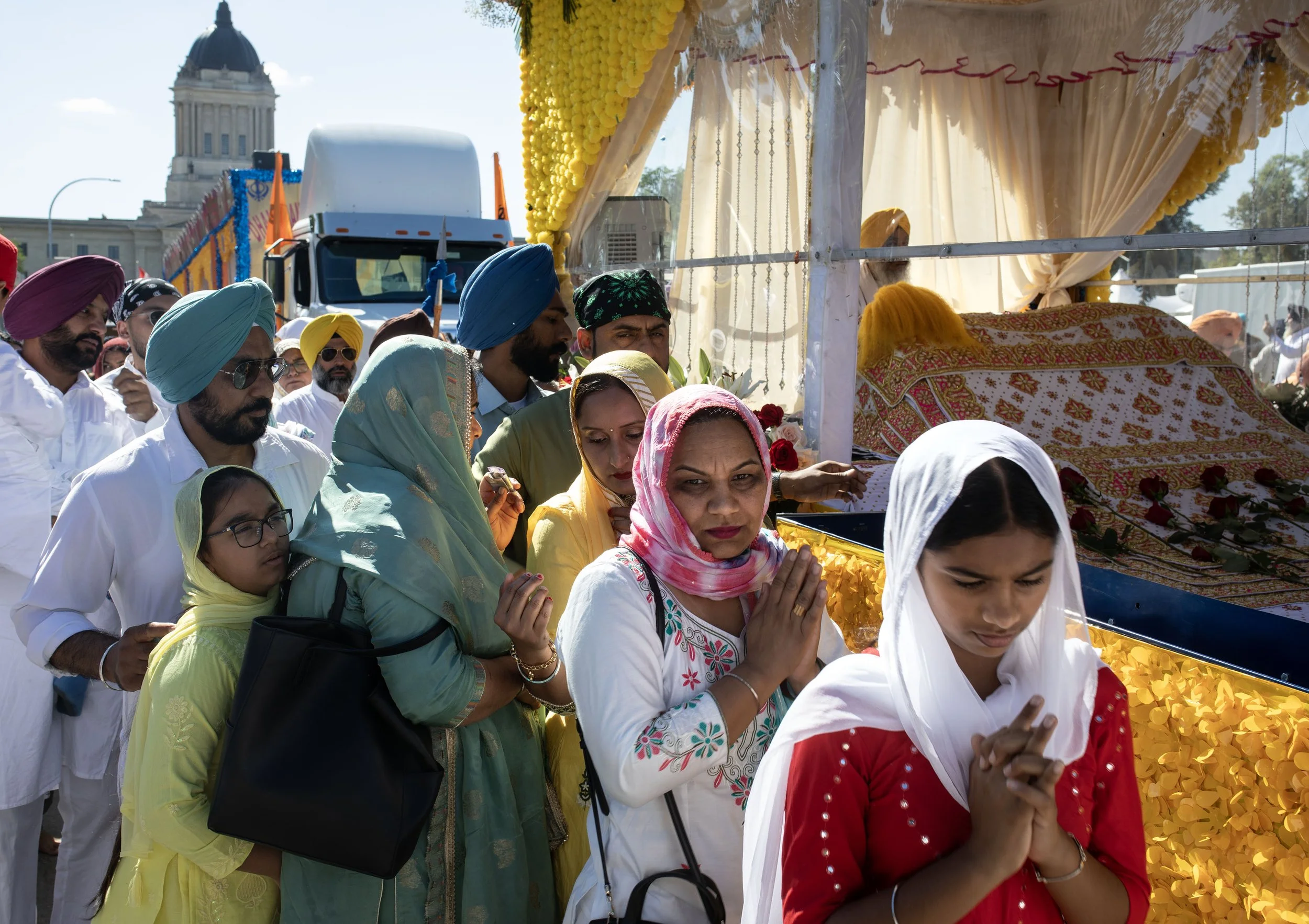 Sikh faithful fold their hands in a prayerful gesture of faith and respect as they walk past the Sri Guru Granth Sahib Ji, or holy book of Sikhism