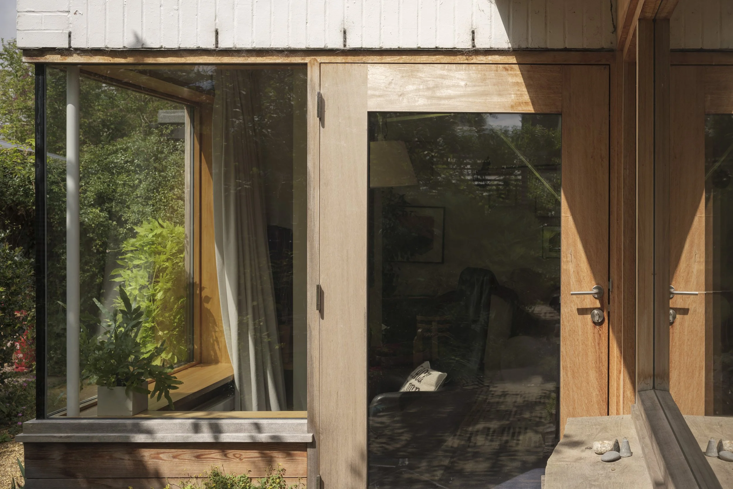 Close-up of modern house window and wooden door with metal handles, surrounded by greenery.