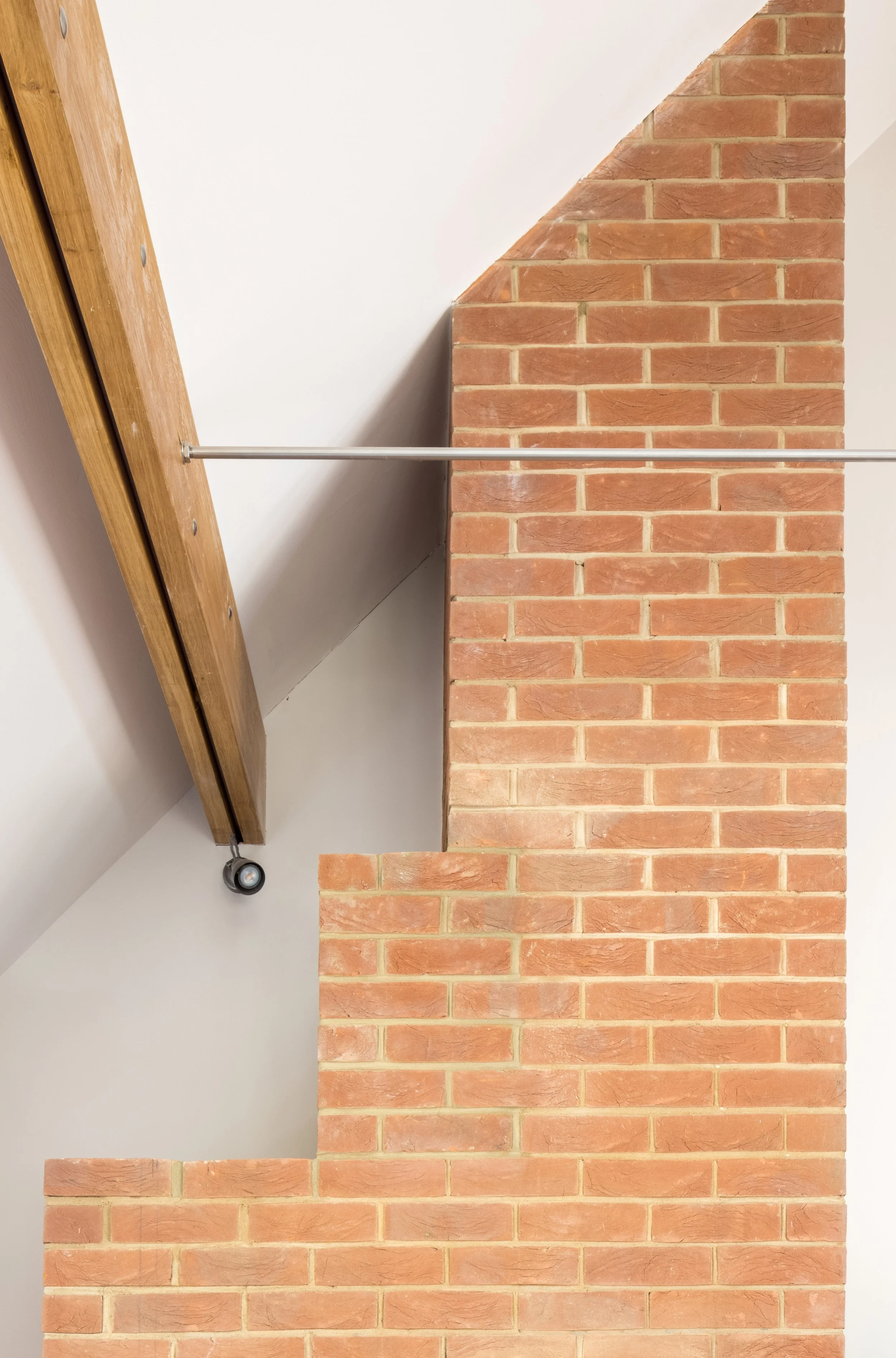 View of a staircase with red brick walls on either side and a wooden handrail attached to the wall on the left side.