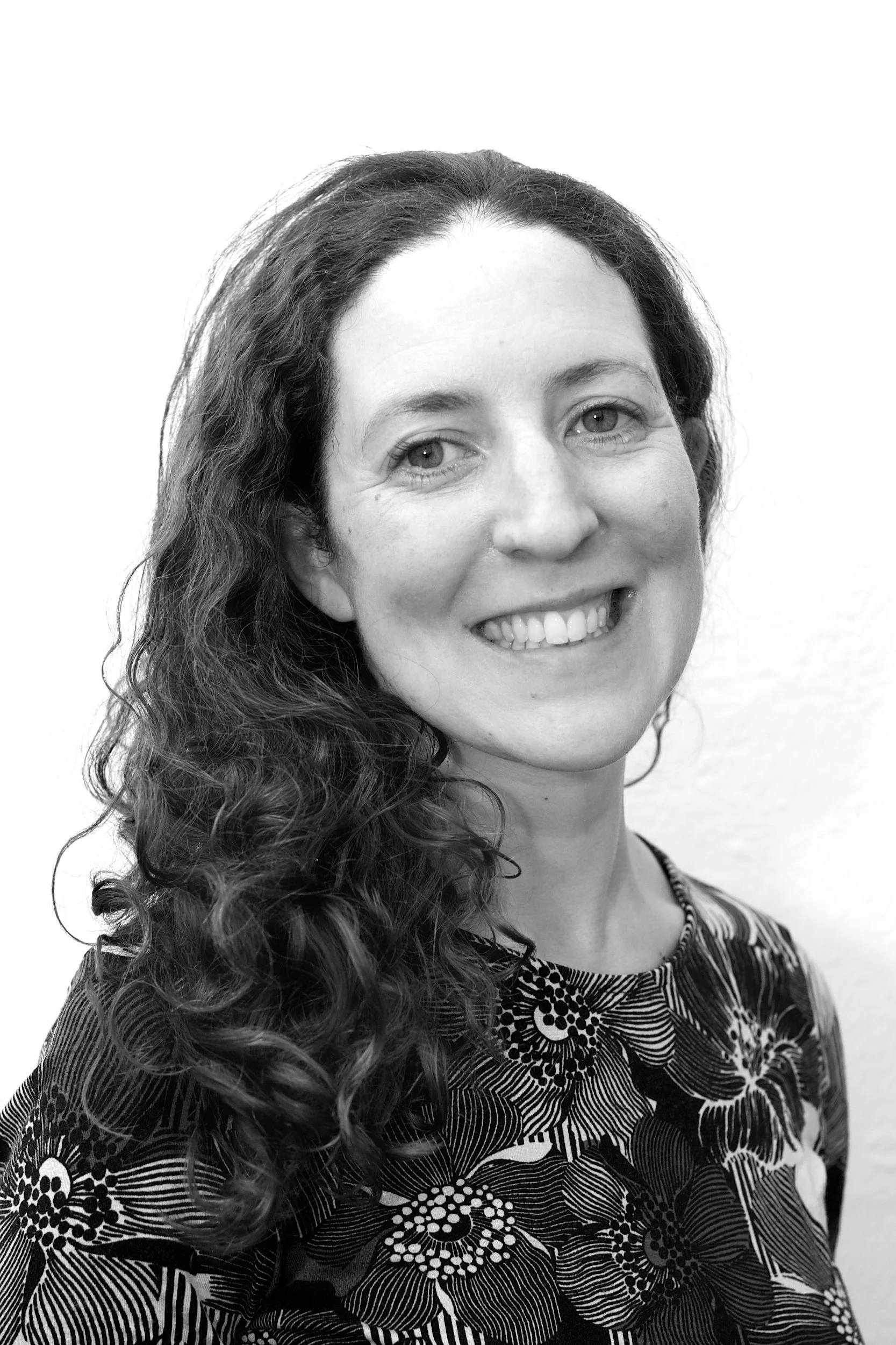 Black and white portrait of a smiling LIz King woman with long curly hair, wearing a patterned top.