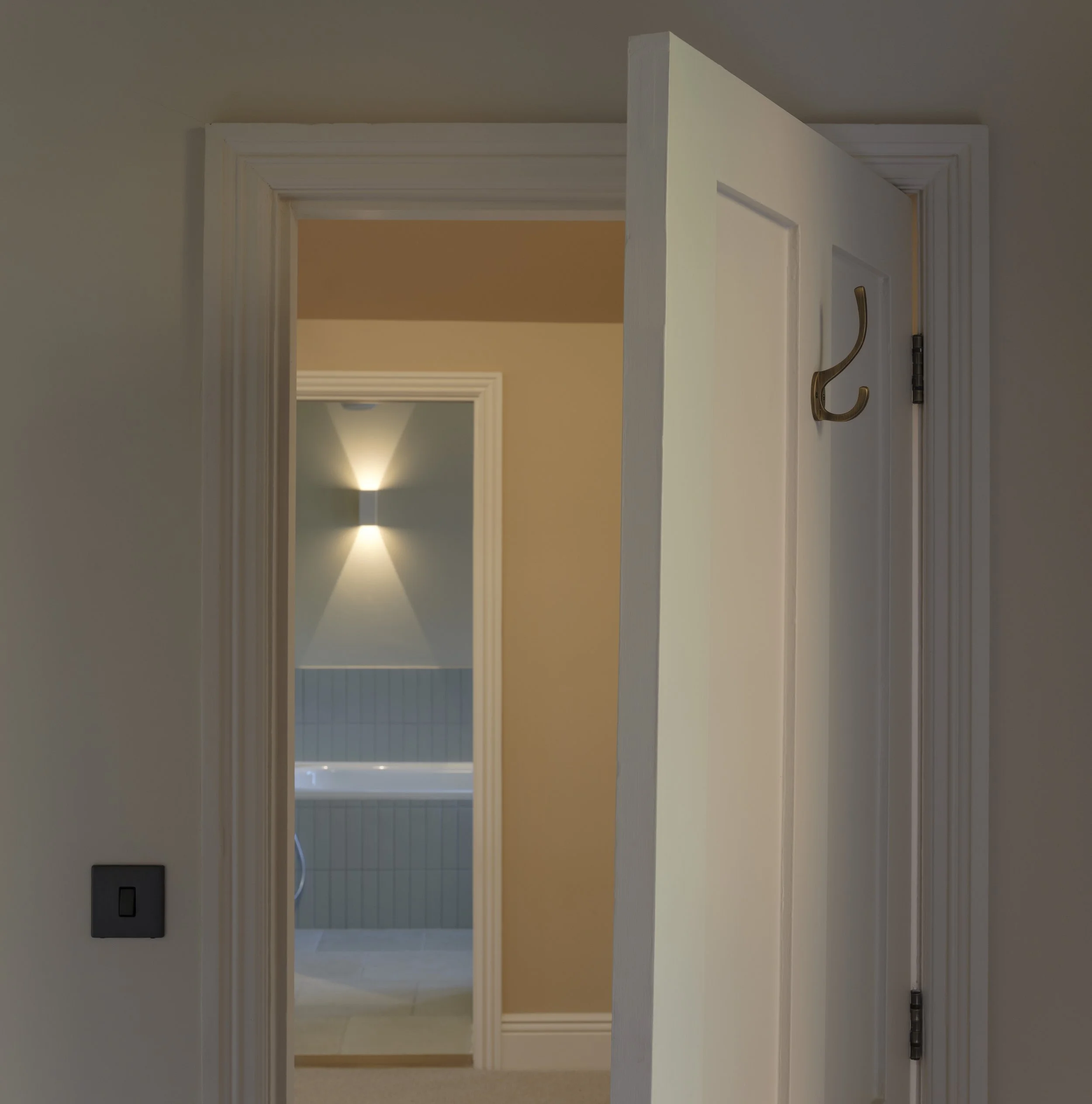 A view of multiple interior doorways leading into rooms with different wall colors, illuminated by ceiling lights, with a light switch and hooks visible on the right side of the foreground door.