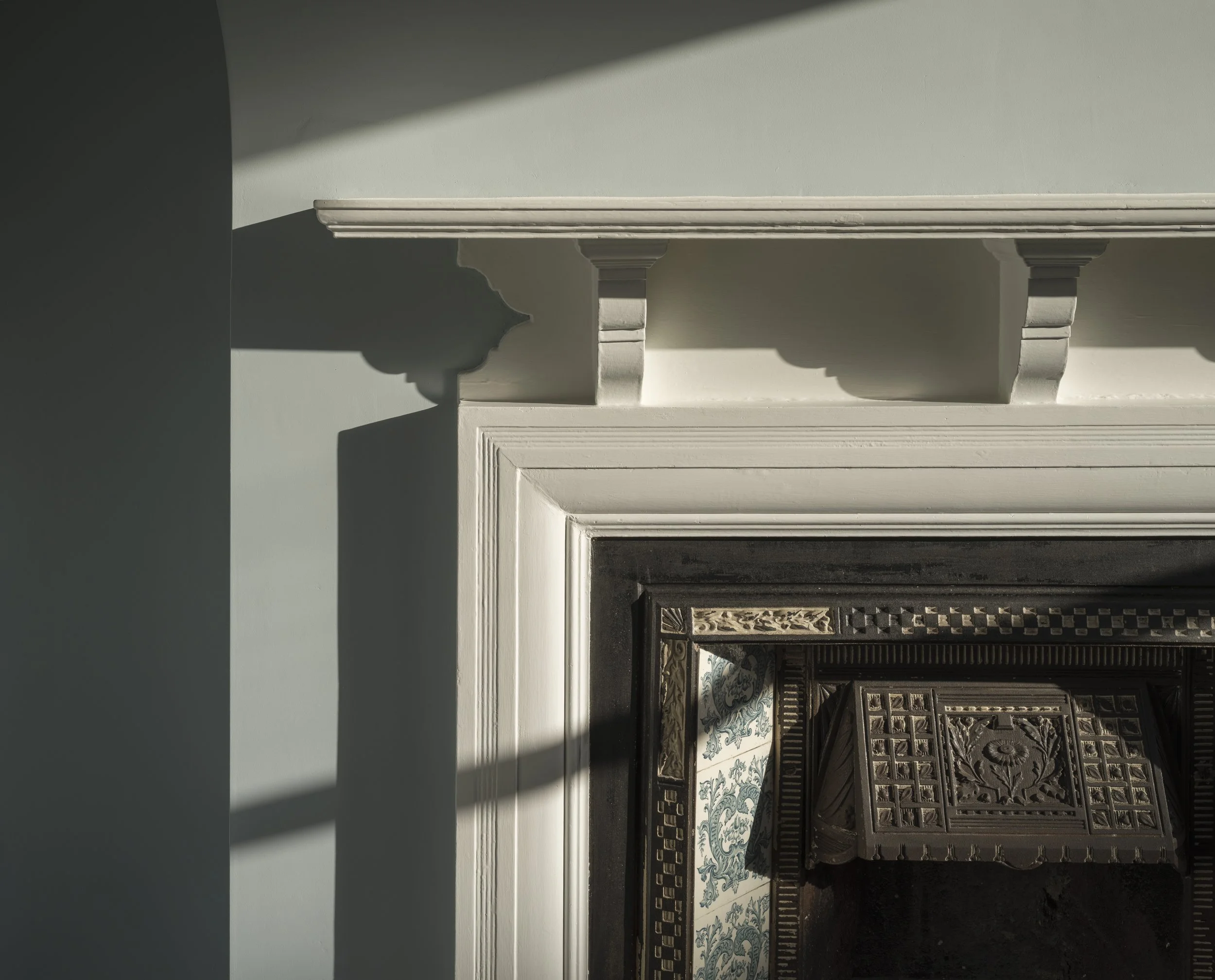 Close-up of a fireplace mantel and decorative details, with shadows cast on a light-colored wall.