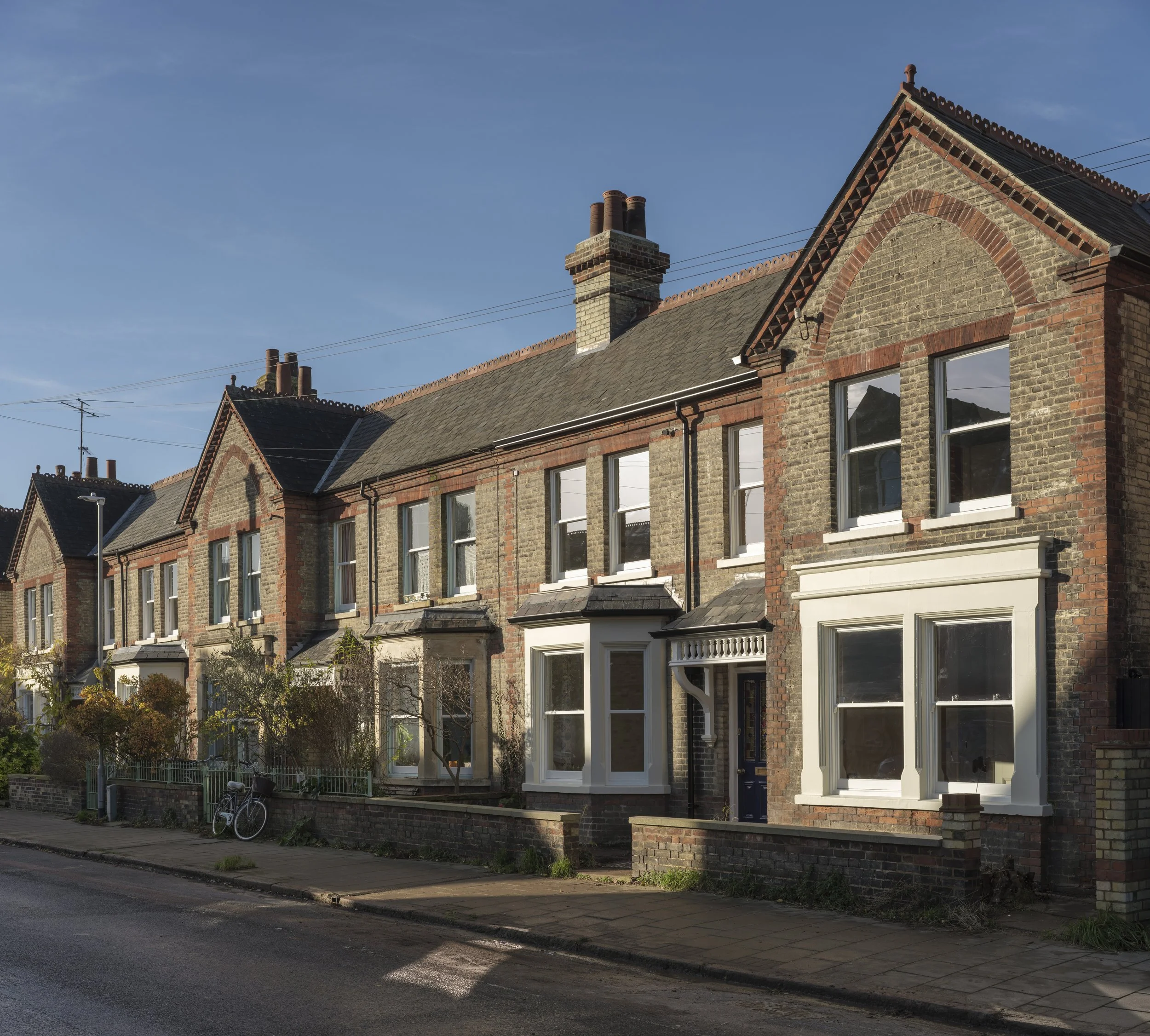 Row of brick houses with large windows, front yards, and chimneys under a clear blue sky.