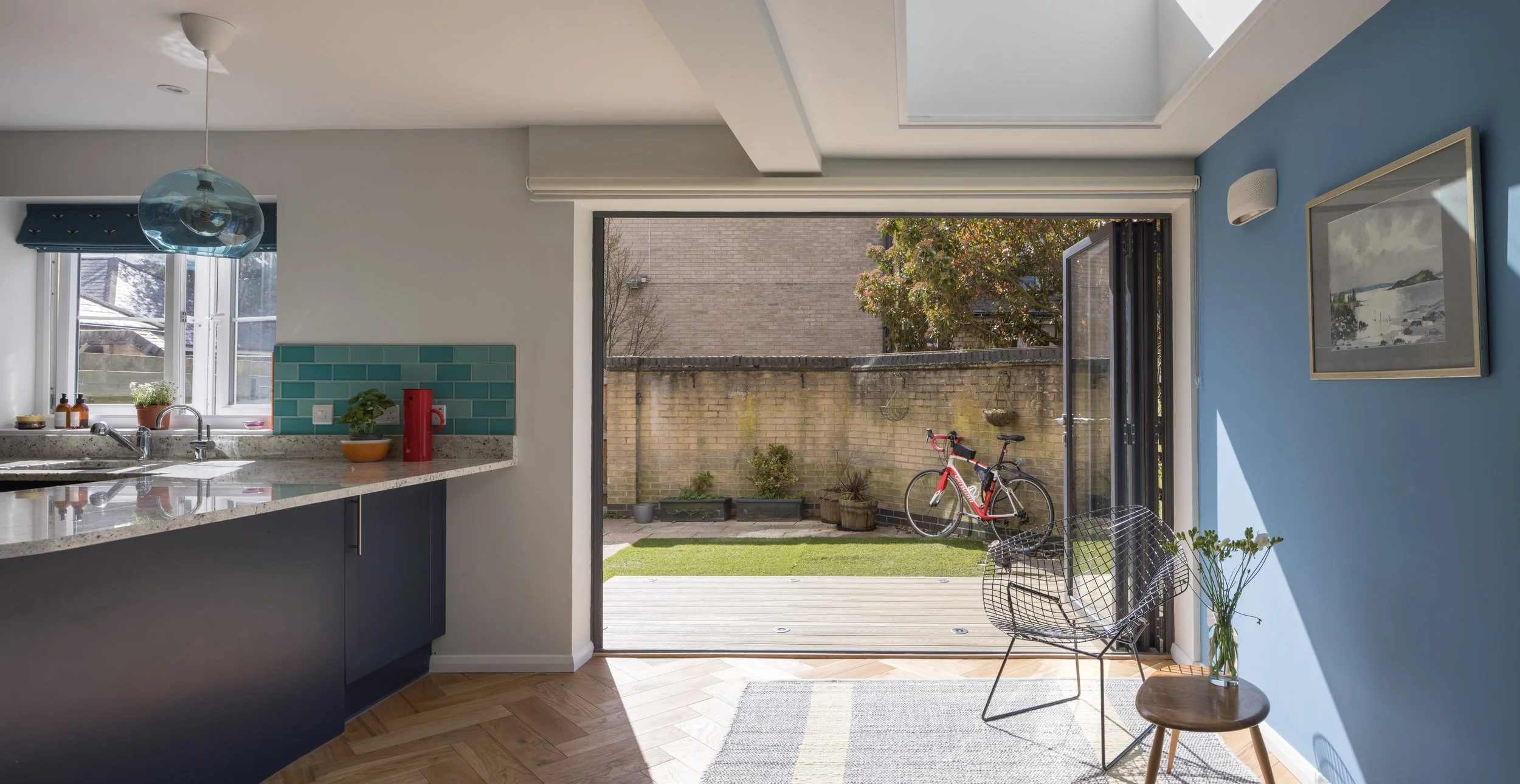 View from inside a kitchen looking out to a backyard patio with a bicycle, small plants, and a brick wall.