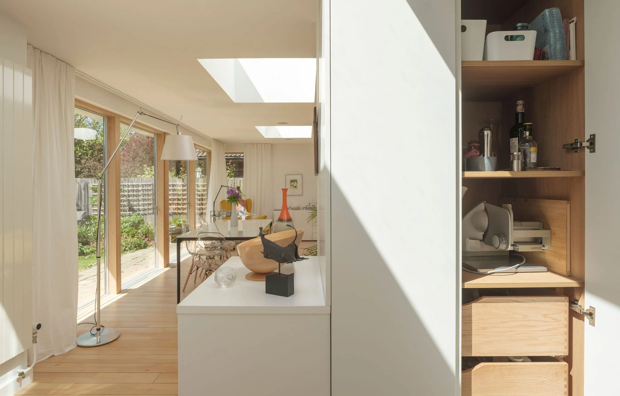 A bright dining area with large sliding glass doors leading to a backyard, featuring a white dining table, a modern floor lamp, and decorative items on the table, with window view of garden and patio.