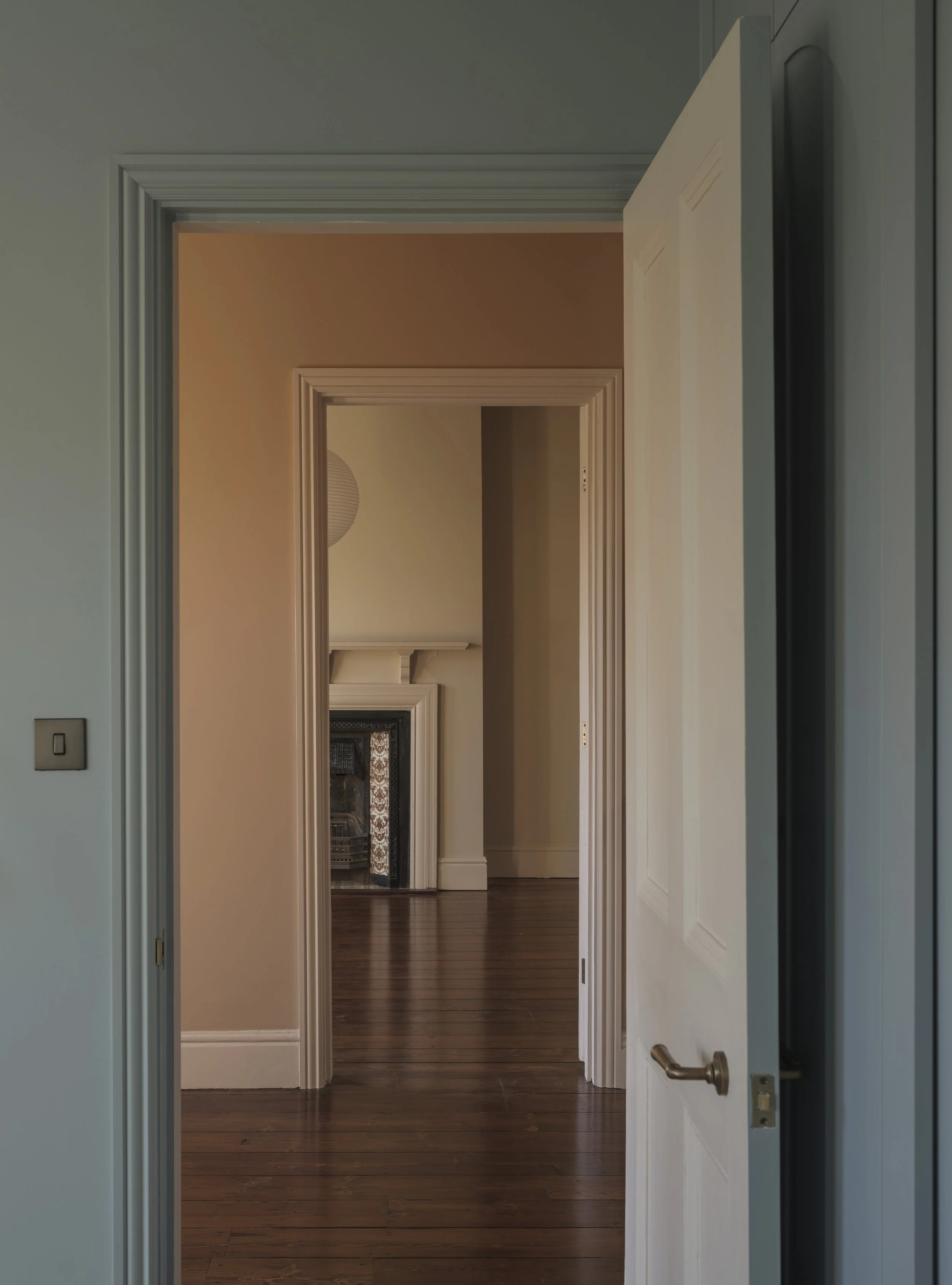 View through multiple open doorways in a house, showing a room with white walls, a staircase, and hardwood floors.