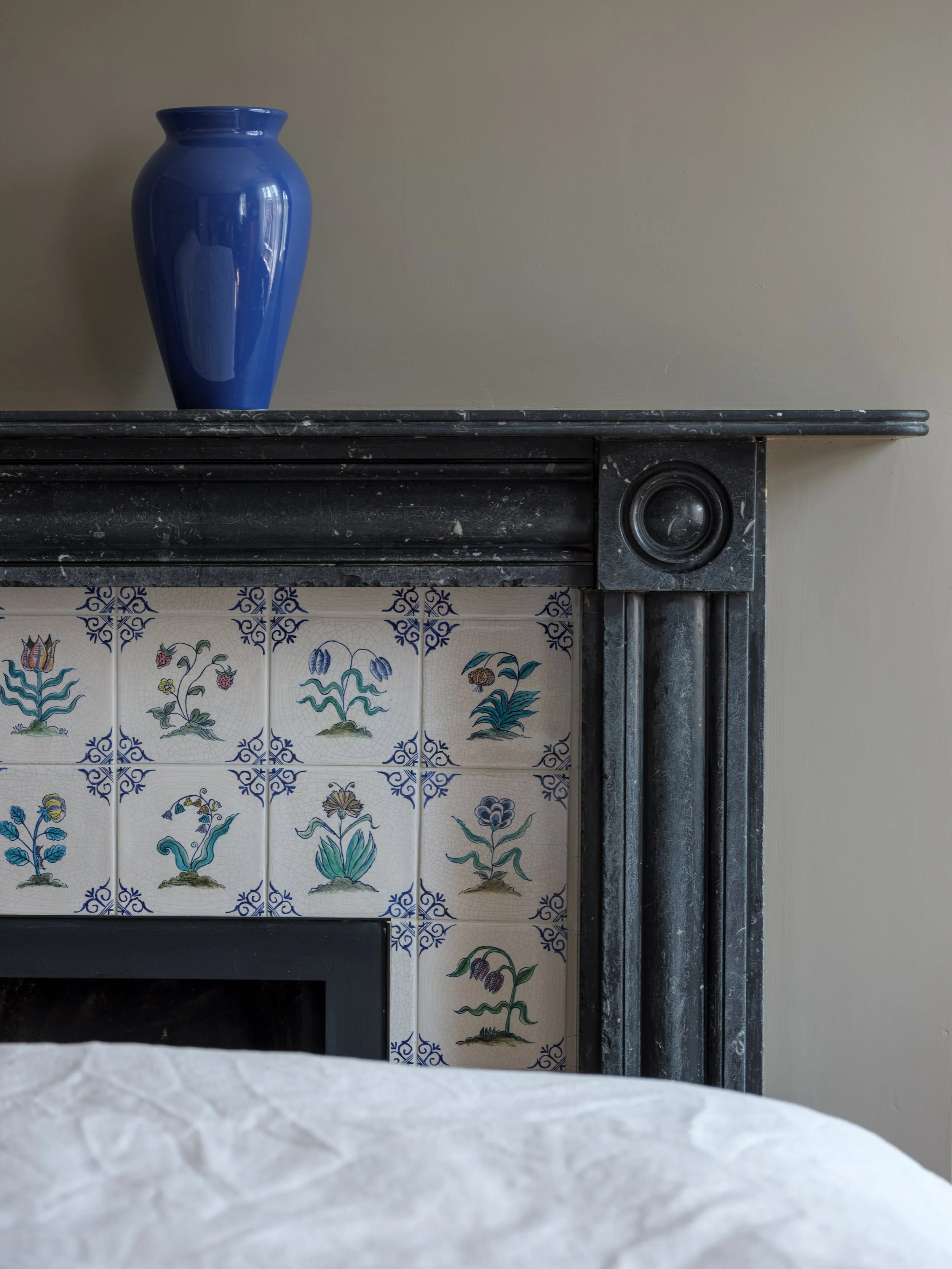 A blue ceramic vase on a black marble mantelpiece against a plain beige wall.