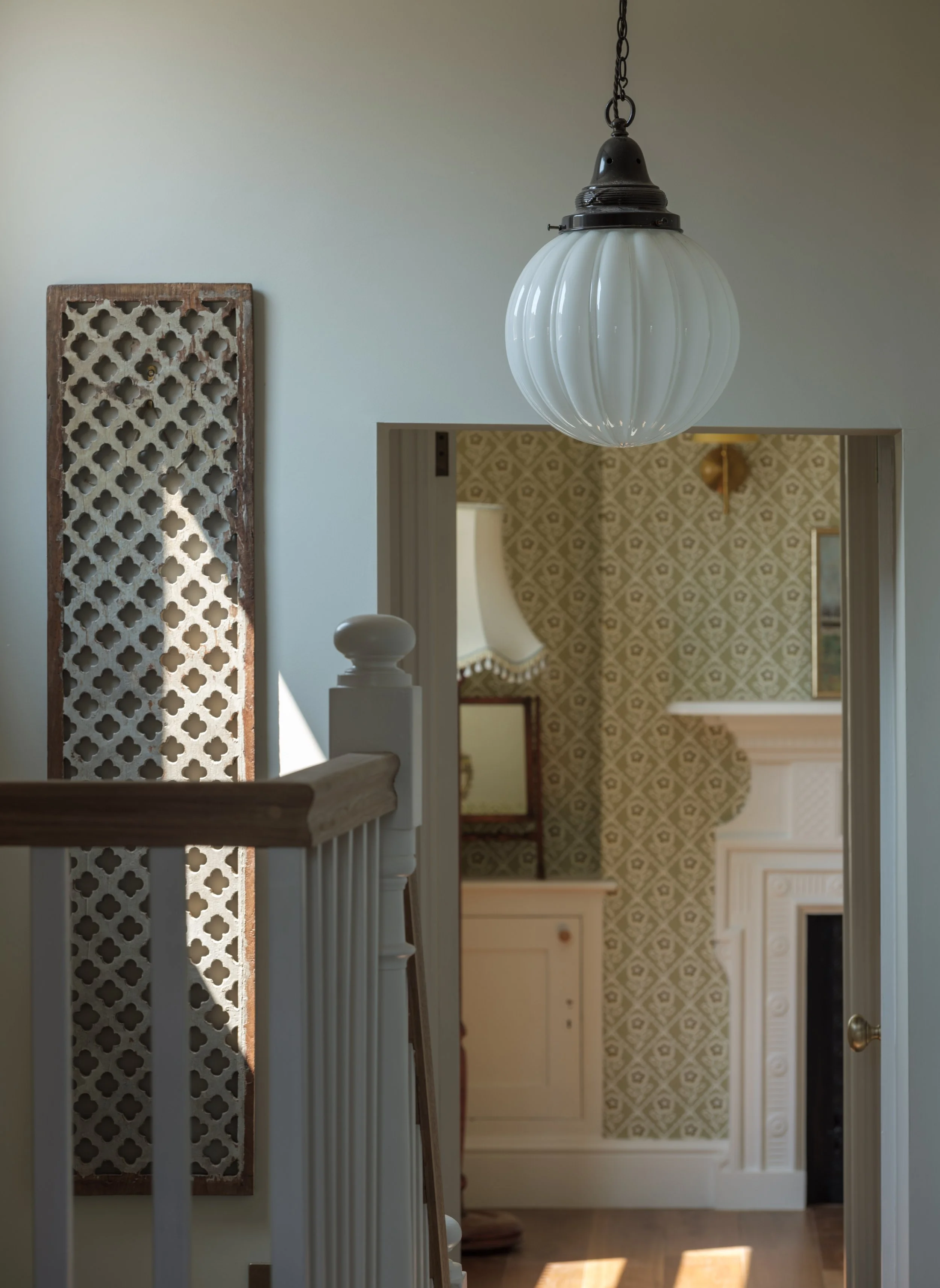 Interior view of a house with a hanging light fixture and a doorway leading to a room with patterned wallpaper.