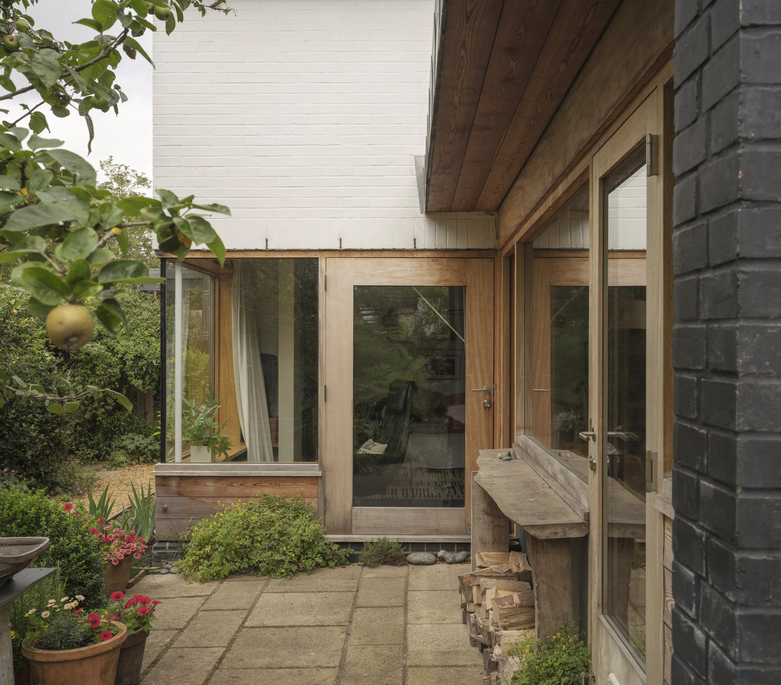Exterior view of a modern house with large glass doors, wooden and brick exterior, and a garden with potted plants and flowers
