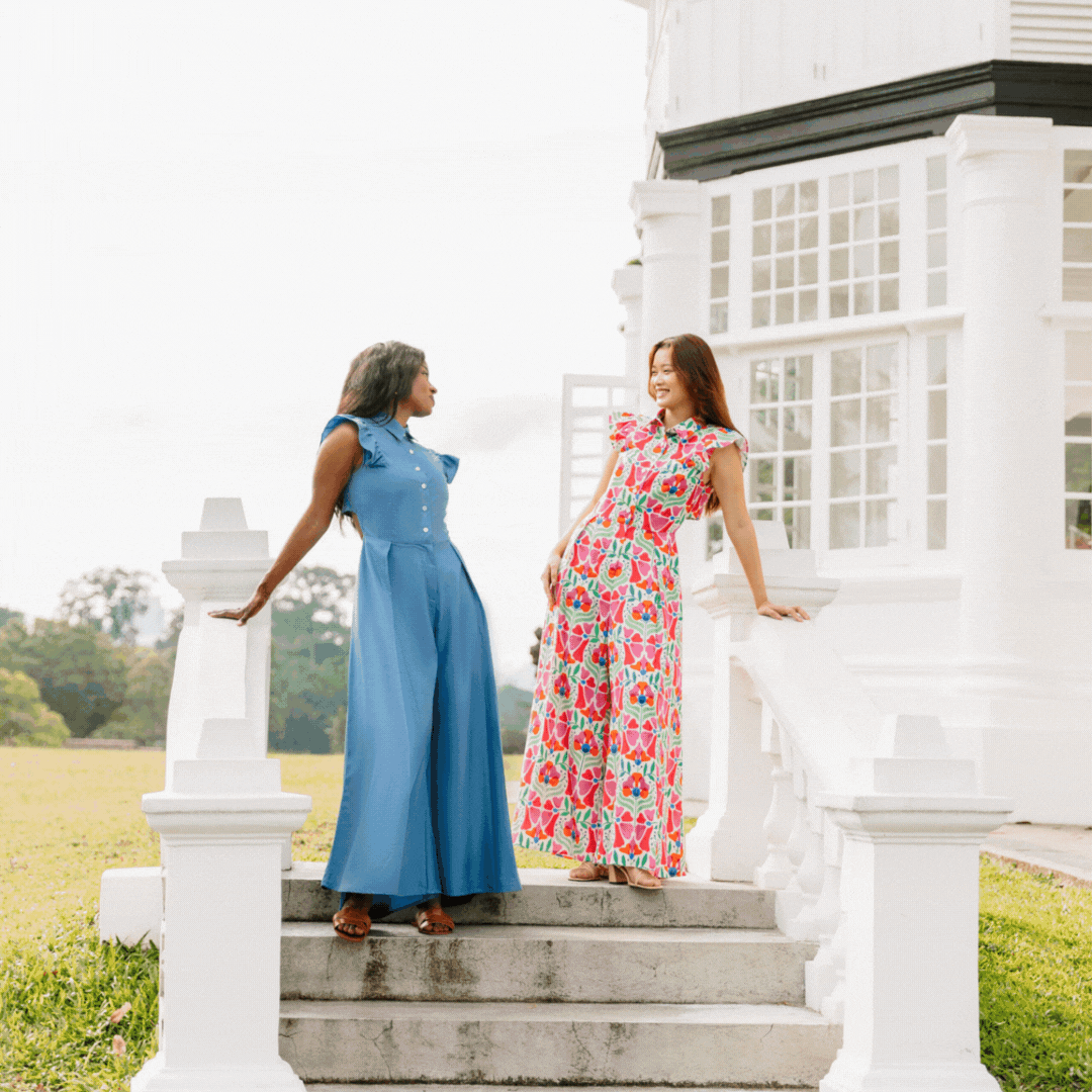 Two women standing on outdoor stairs by a white building, smiling and talking to each other.
