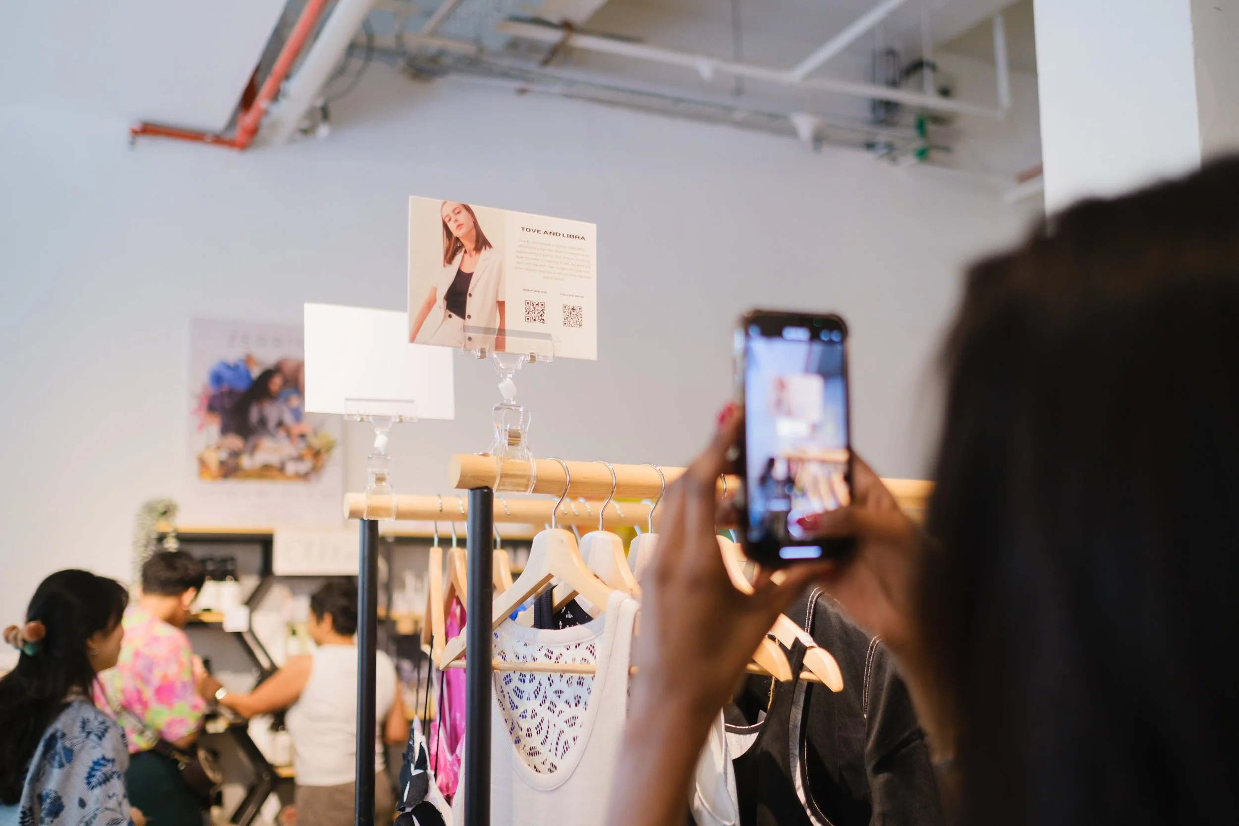A person taking a photo with a smartphone in a retail store with clothing on display and promotional signs.