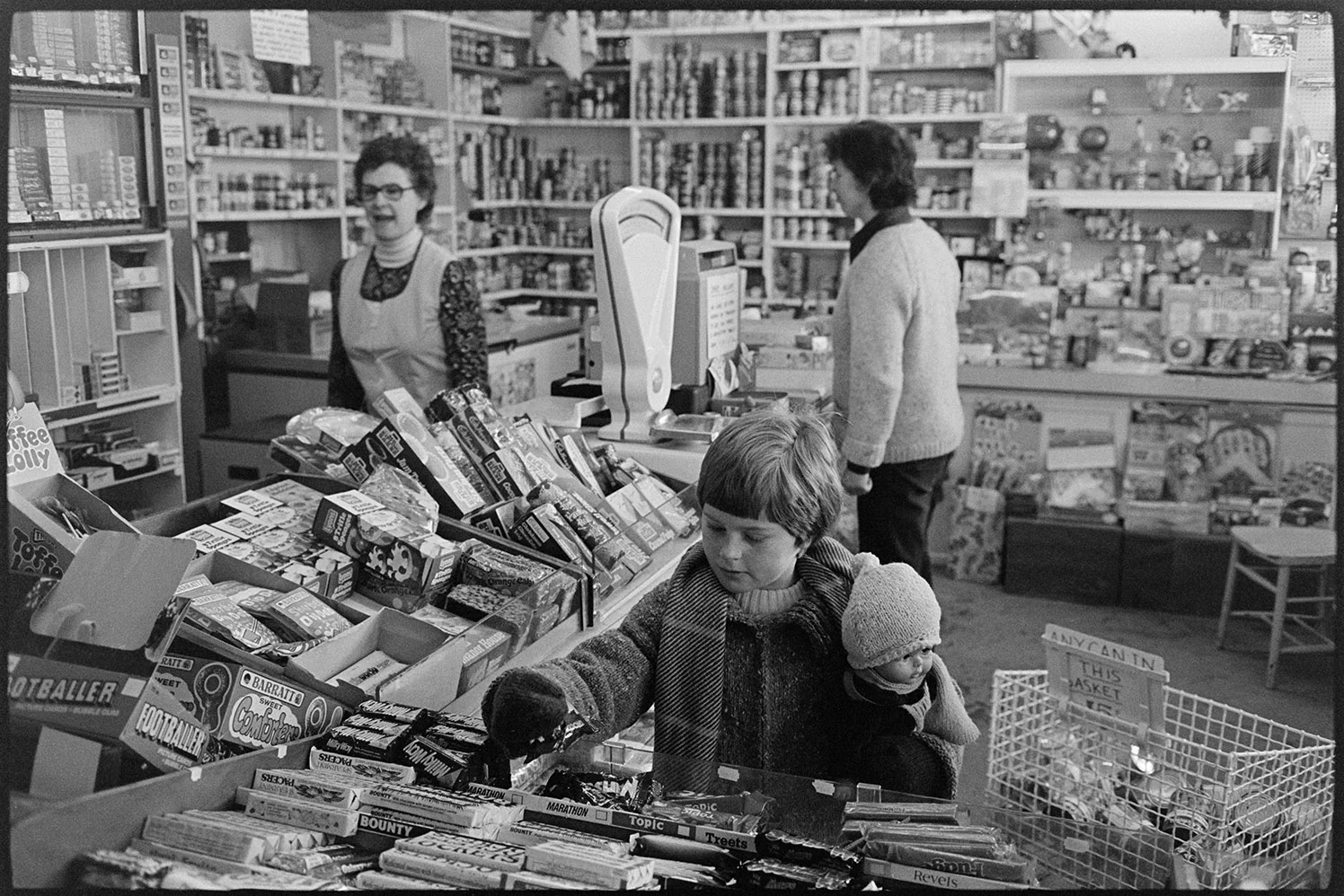 Interior of village grocery stores with customers, child buying sweets, Black Torrington, December 1979