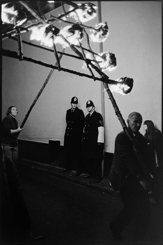 Policemen watching the carnival procession at night, Hatherleigh, 6 November 1974