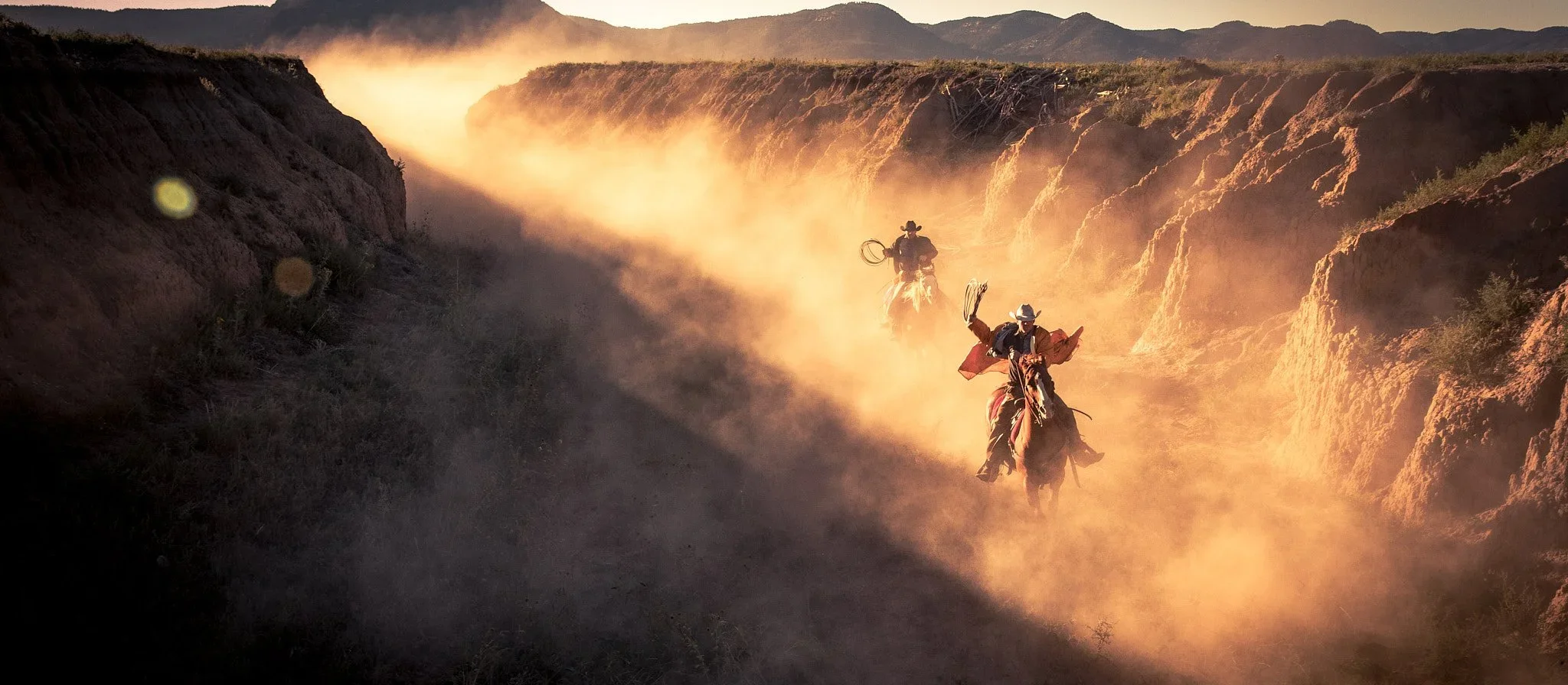 Cowboys riding through canyon dust at sunset in a cinematic western lifestyle campaign scene