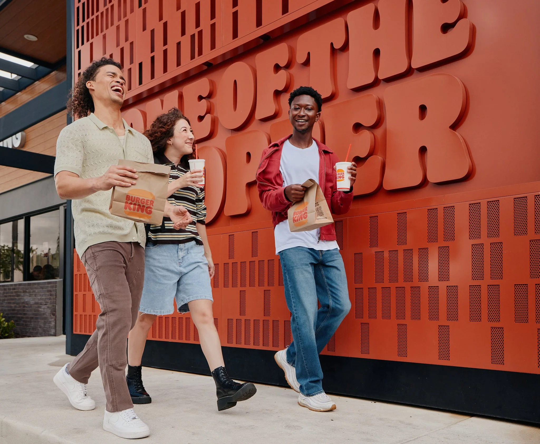 Three friends walking outside Burger King in front of the red Home of the Whopper wall.