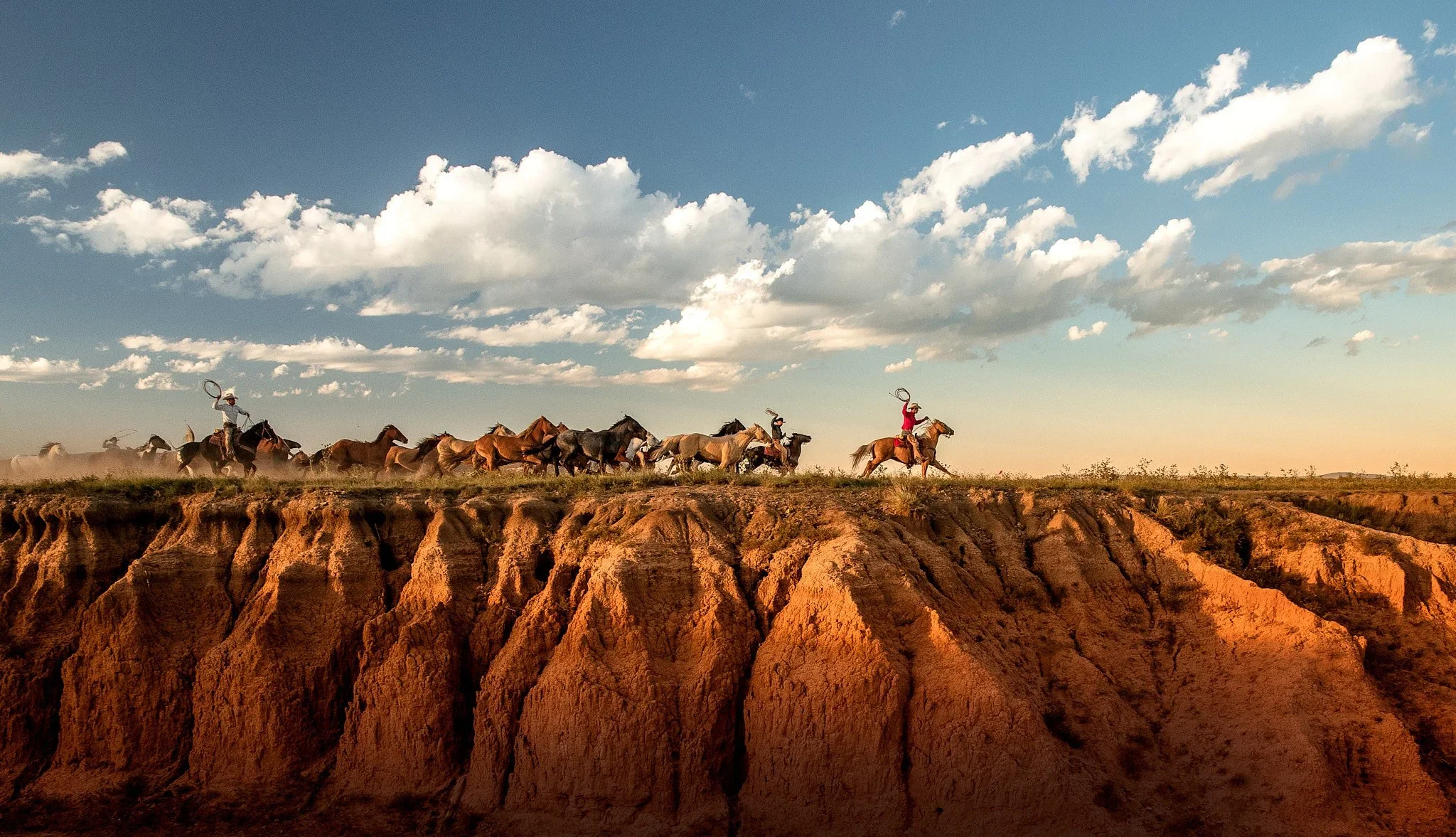 Cowboys driving herd of horses across desert cliffs at golden hour – cinematic western photography by George Kamper