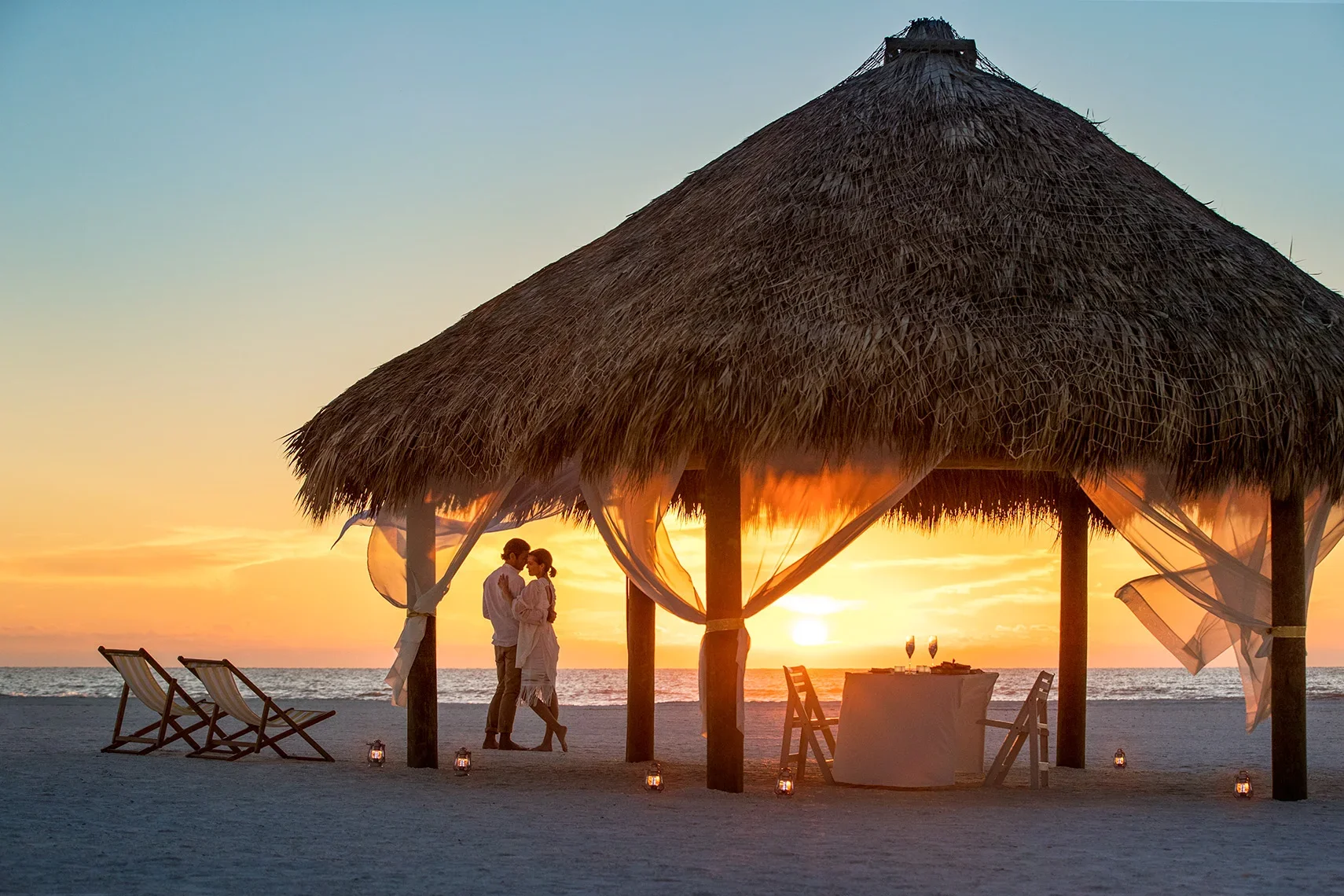 Couple enjoying a romantic sunset dinner beneath a tiki hut photographed for the Love, Paradise campaign for Collier County Tourism on Florida’s Paradise Coast.